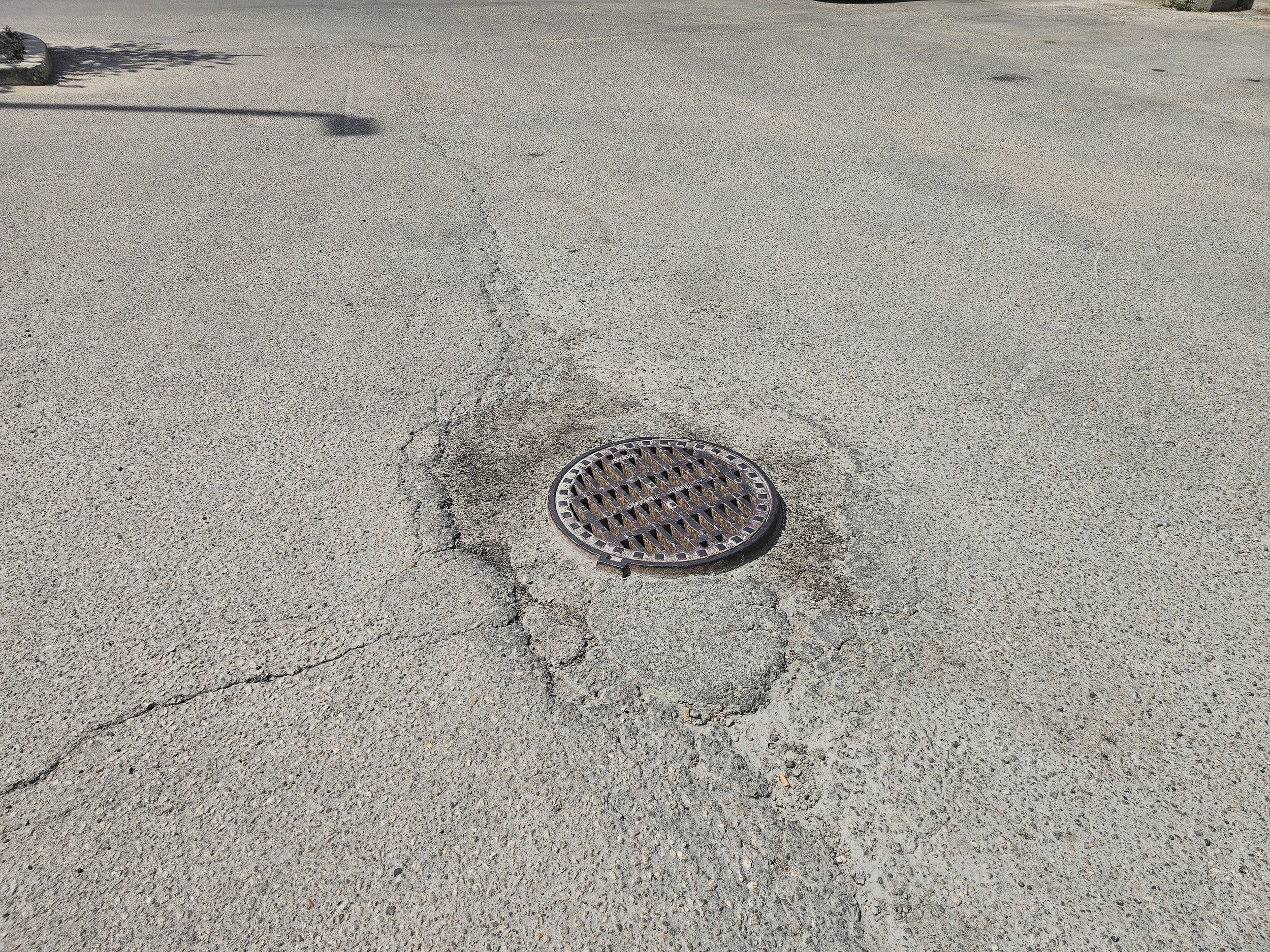 Parking lot pavement with a manhole / drain surrounded by cracked asphalt.