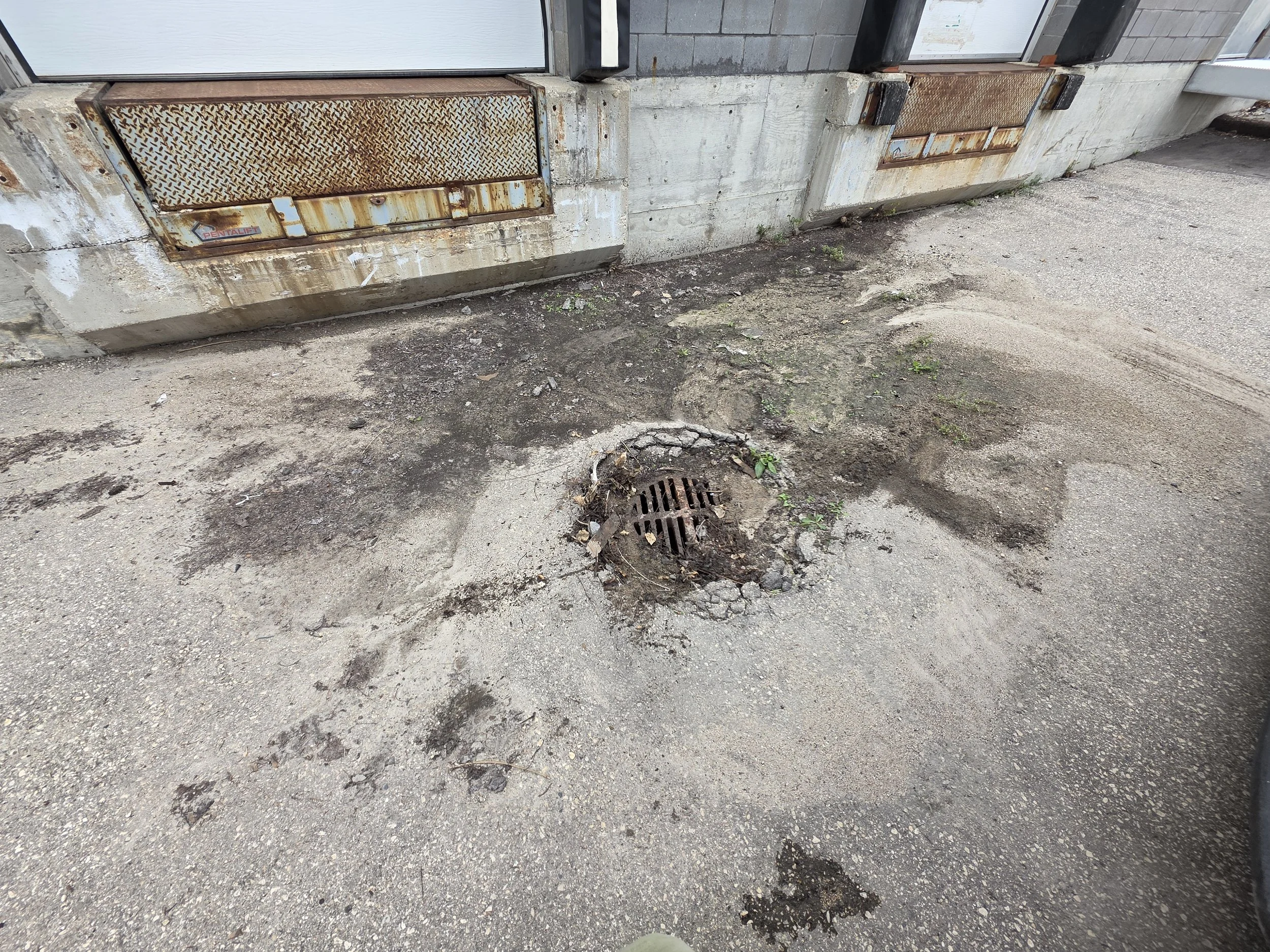 Parking lot pavement with a manhole / drain surrounded by cracked asphalt.