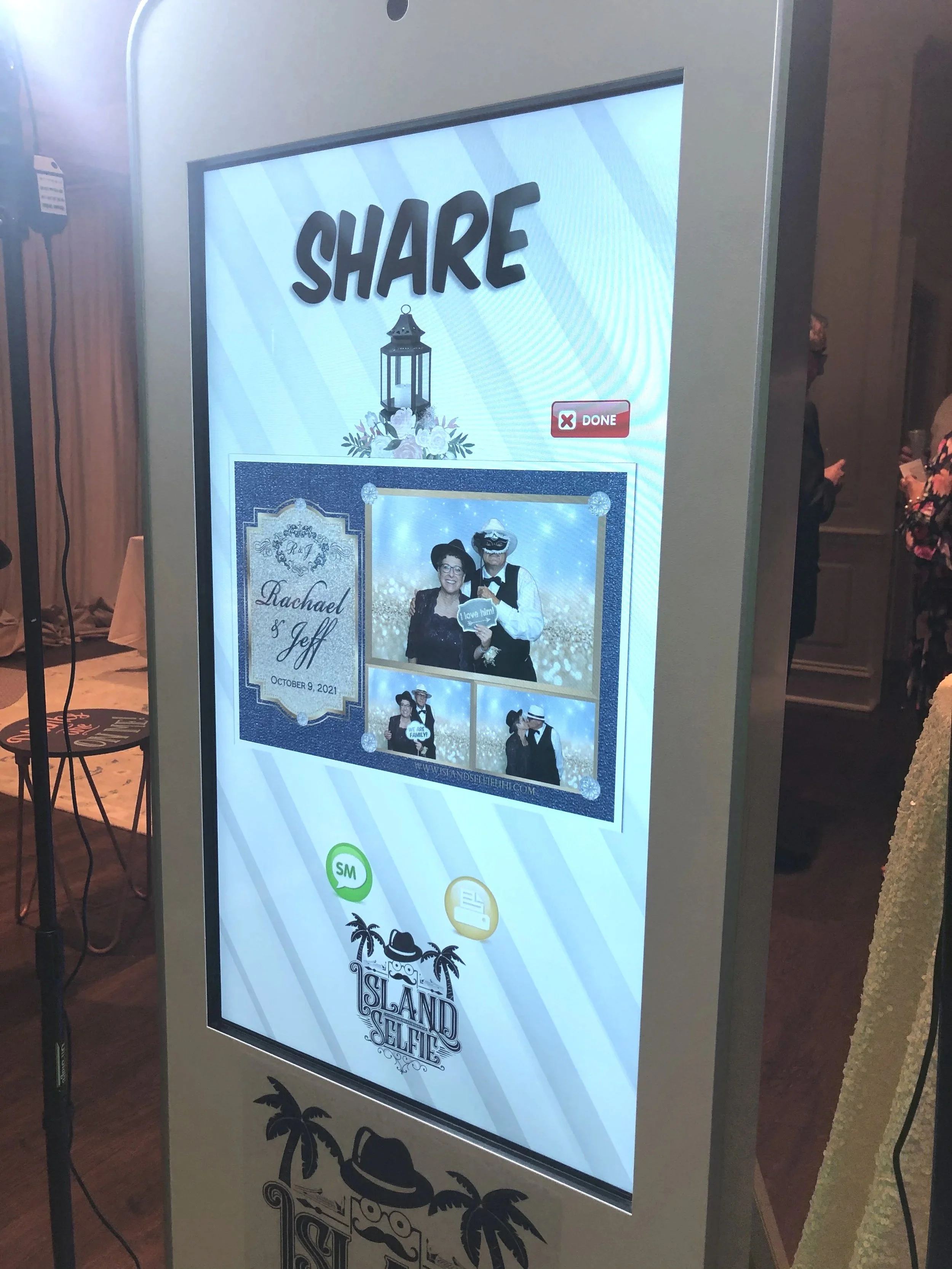 Digital screen displaying a photo booth template with the word 'SHARE' at the top, a lantern graphic, and photos of people in costumes, with a tropical island theme logo at the bottom.