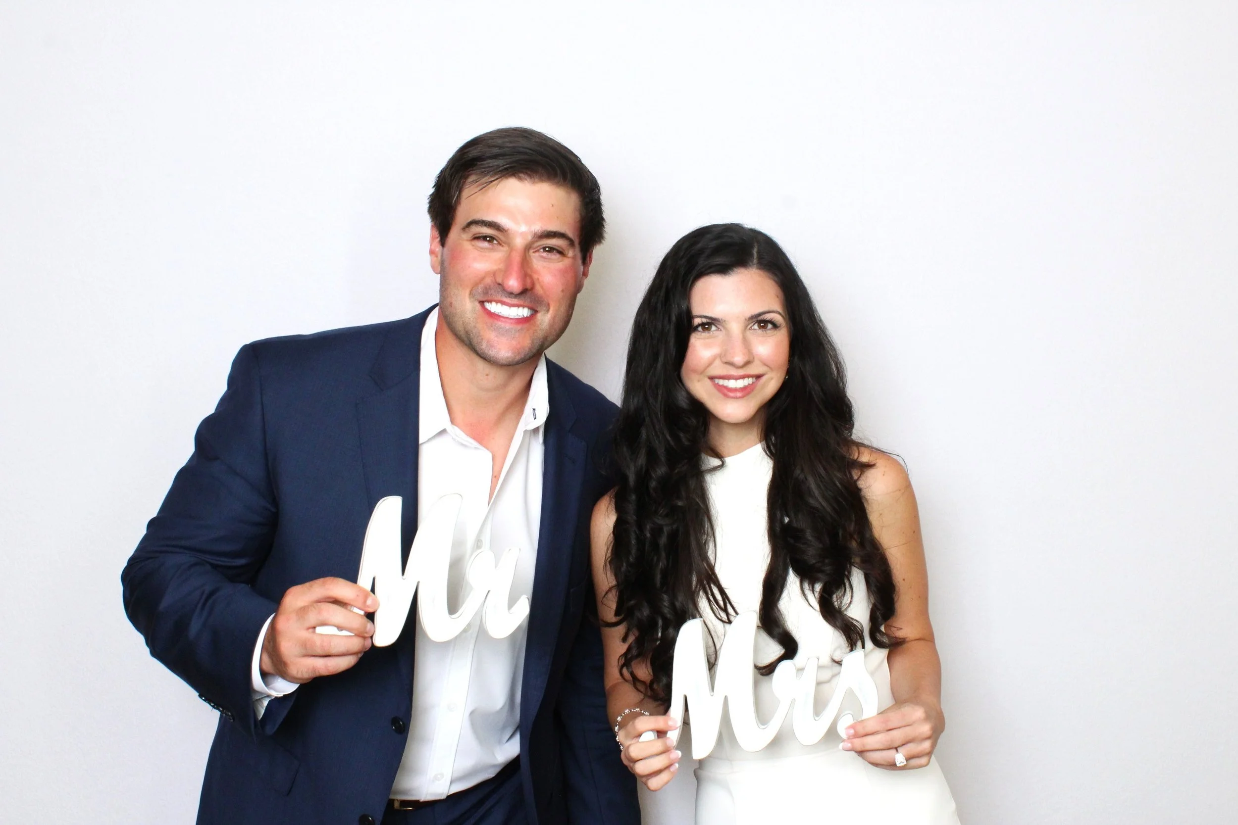 A man and woman smiling, dressed in formal attire, holding white signs that say 'Mr' and 'Mrs'.