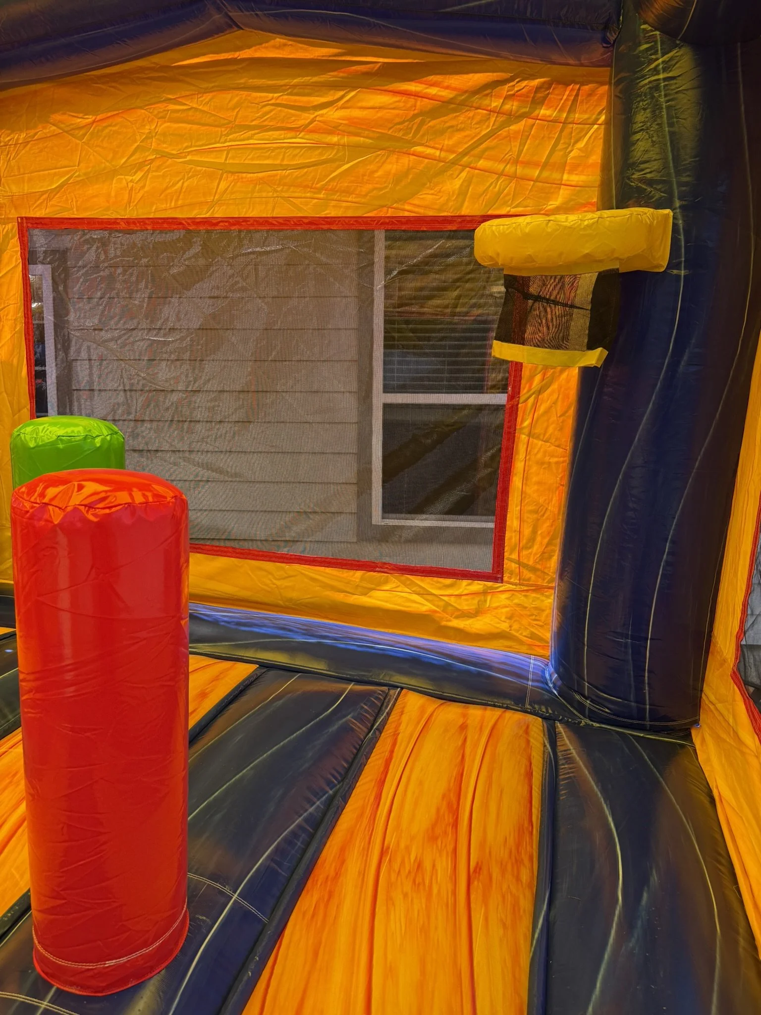 Inside view of an orange and black inflatable bounce house with red and green soft poles and a small yellow cushion on the side.