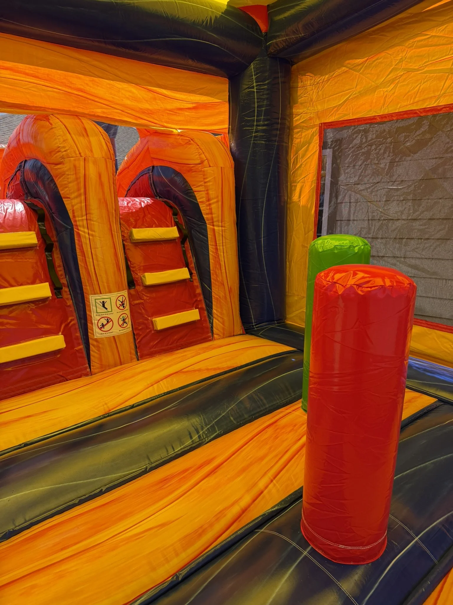 Interior of an inflatable bounce house with orange, black, green, and yellow colors, featuring climbing sections and padded columns for safety.