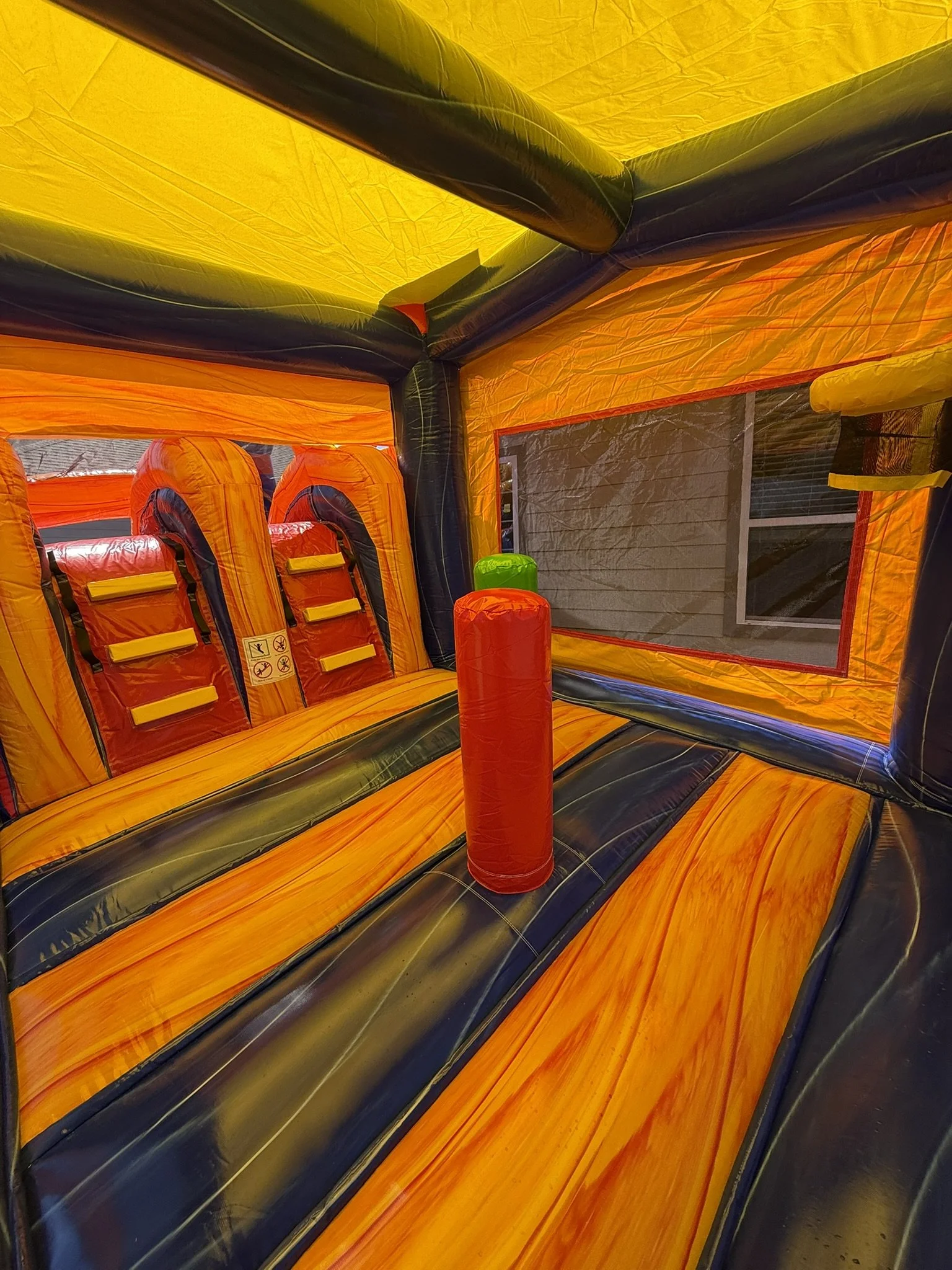 Interior of a colorful inflatable bounce house with orange, yellow, black, and green sections, including a red padded obstacle and mesh windows.