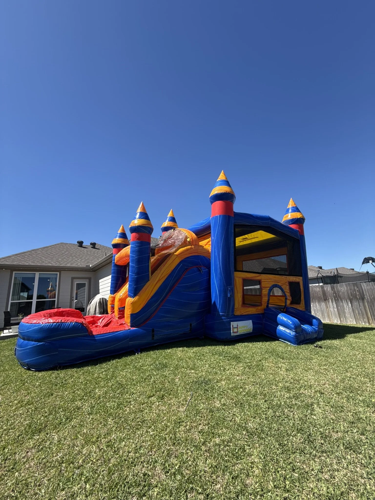 Colorful inflatable bounce house with a slide in a backyard on a sunny day.
