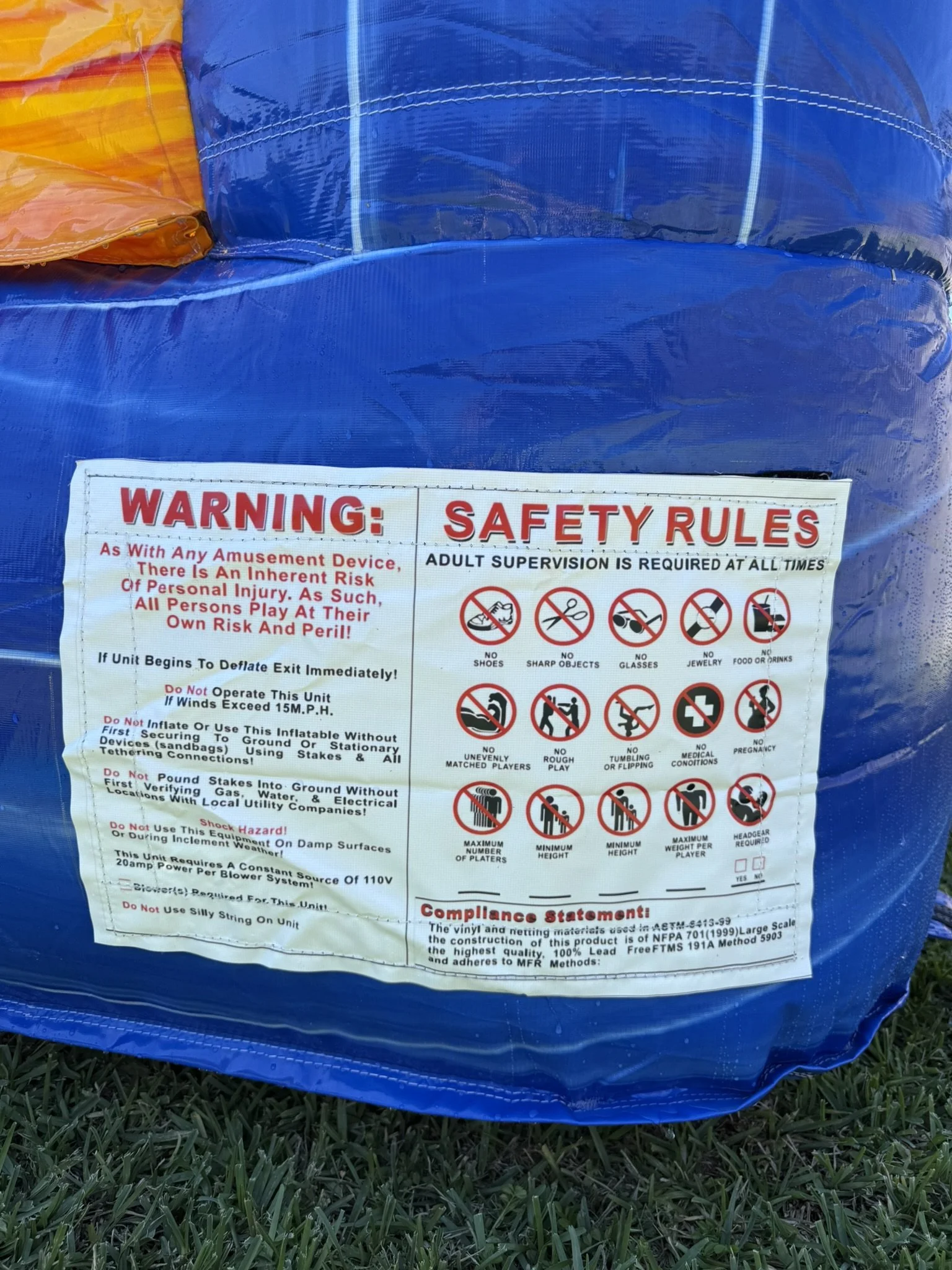 Warning and safety rules sticker on a blue inflatable, with icons indicating no shoes, no sharp objects, no glasses, no jewelry, no food or drinks, no unevenly matched players, no rough play, no tumbling or flipping, no medical conditions, no pregnan