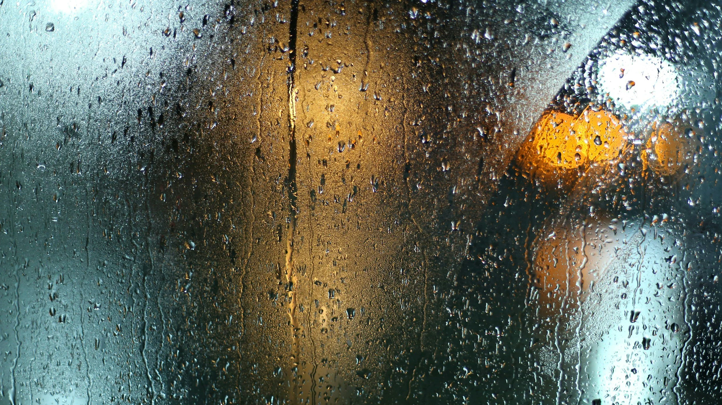 Rain-covered window with blurred city lights visible through the glass.