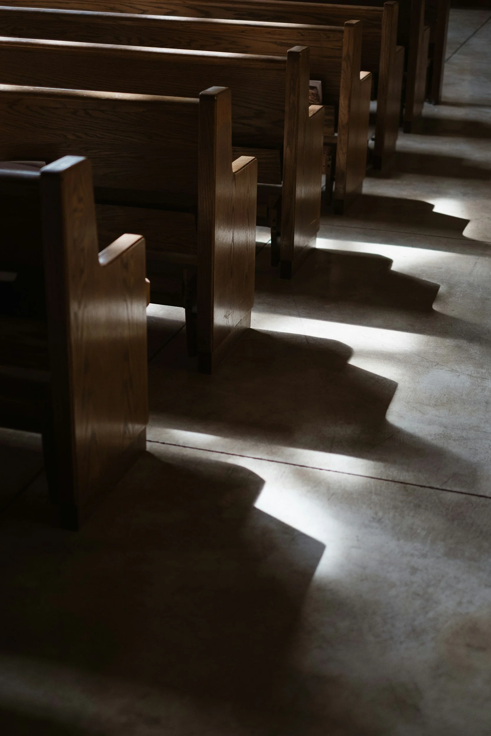 Empty wooden church pews casting shadows on the floor, illuminated by natural light.