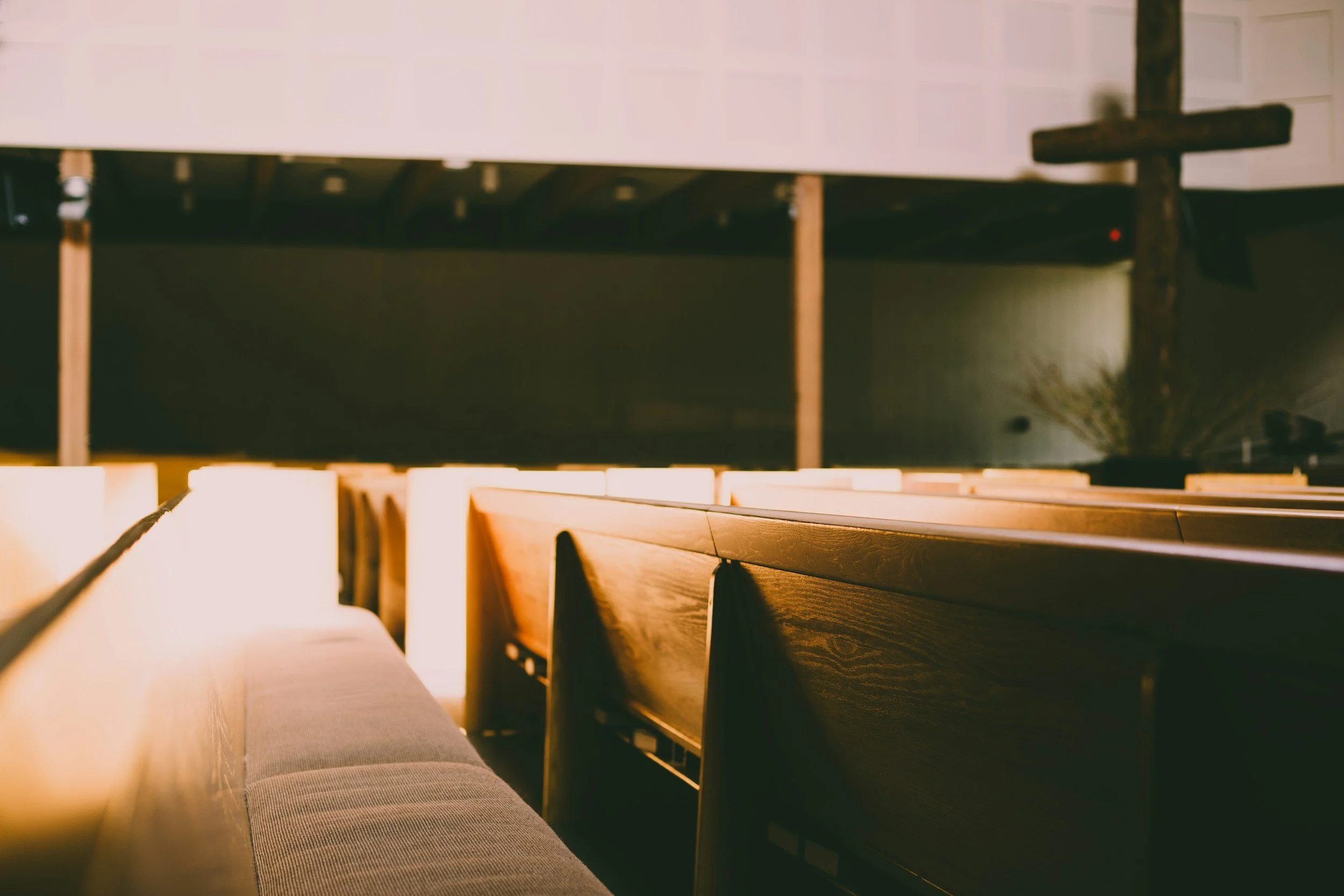 Interior of a church or chapel with wooden pews and a wooden cross on the wall.