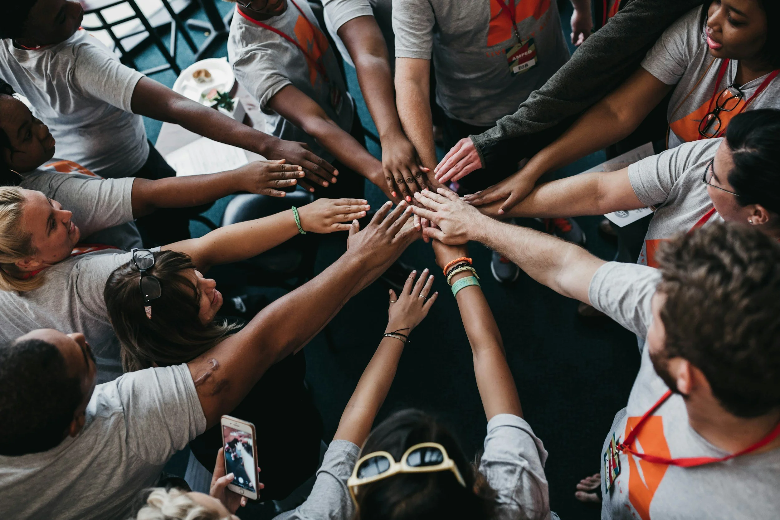 Group of diverse people participating in a team activity with their hands stacked in the center, symbolizing unity and teamwork at a conference or workshop.