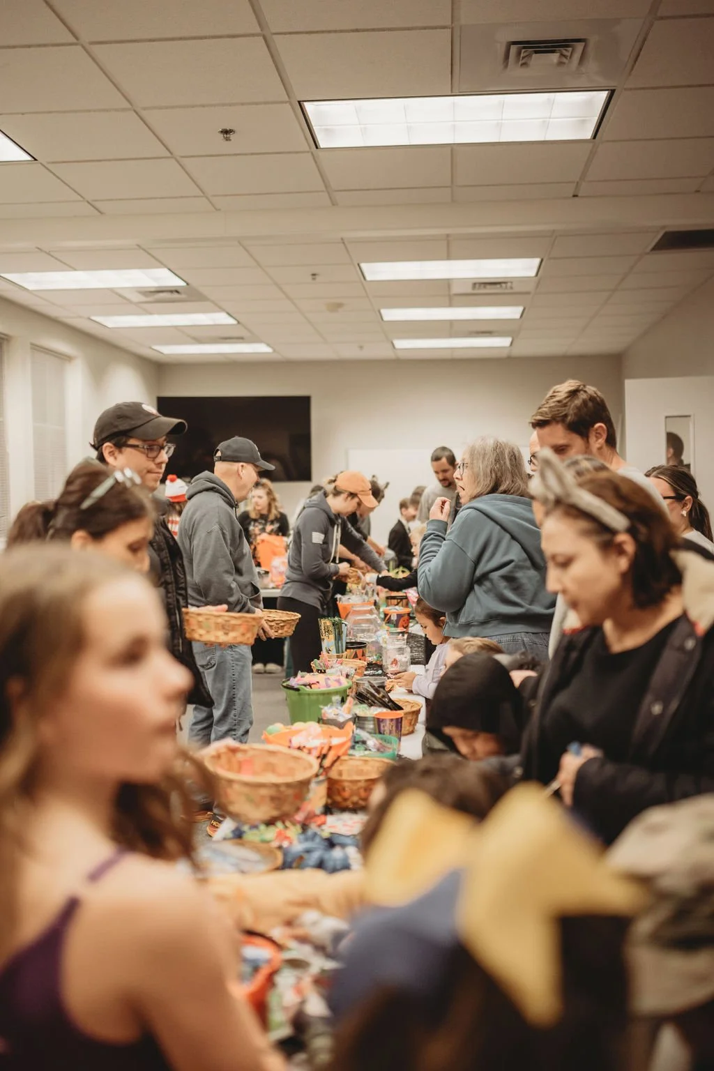 People gathered around tables with baskets and treats at a crowded indoor event.