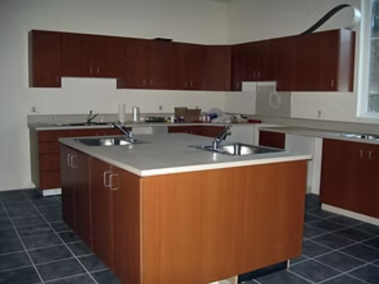 Empty kitchen with wooden cabinets, a center island with double sinks, and tiled black flooring.