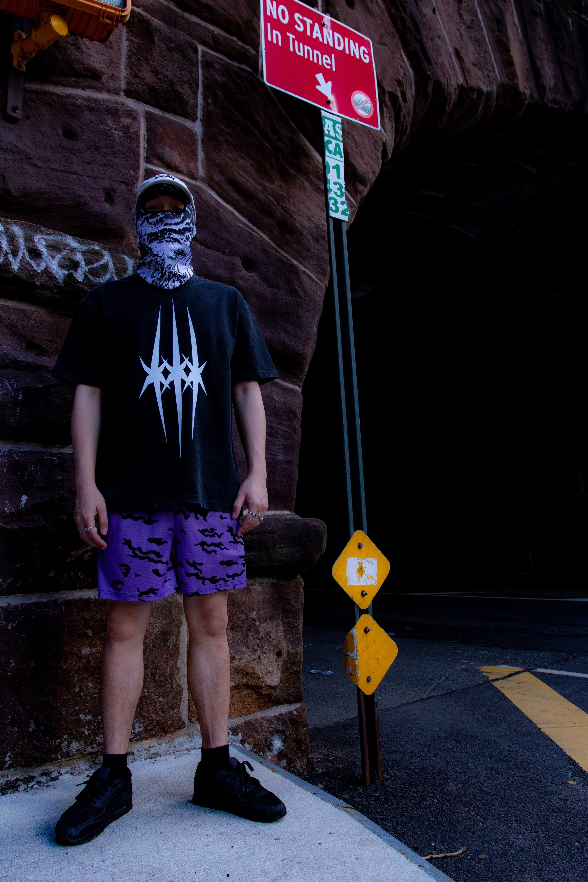 Person standing next to a sign that reads 'No Standing In Tunnel,' with a separate yellow caution sign on a traffic post nearby.