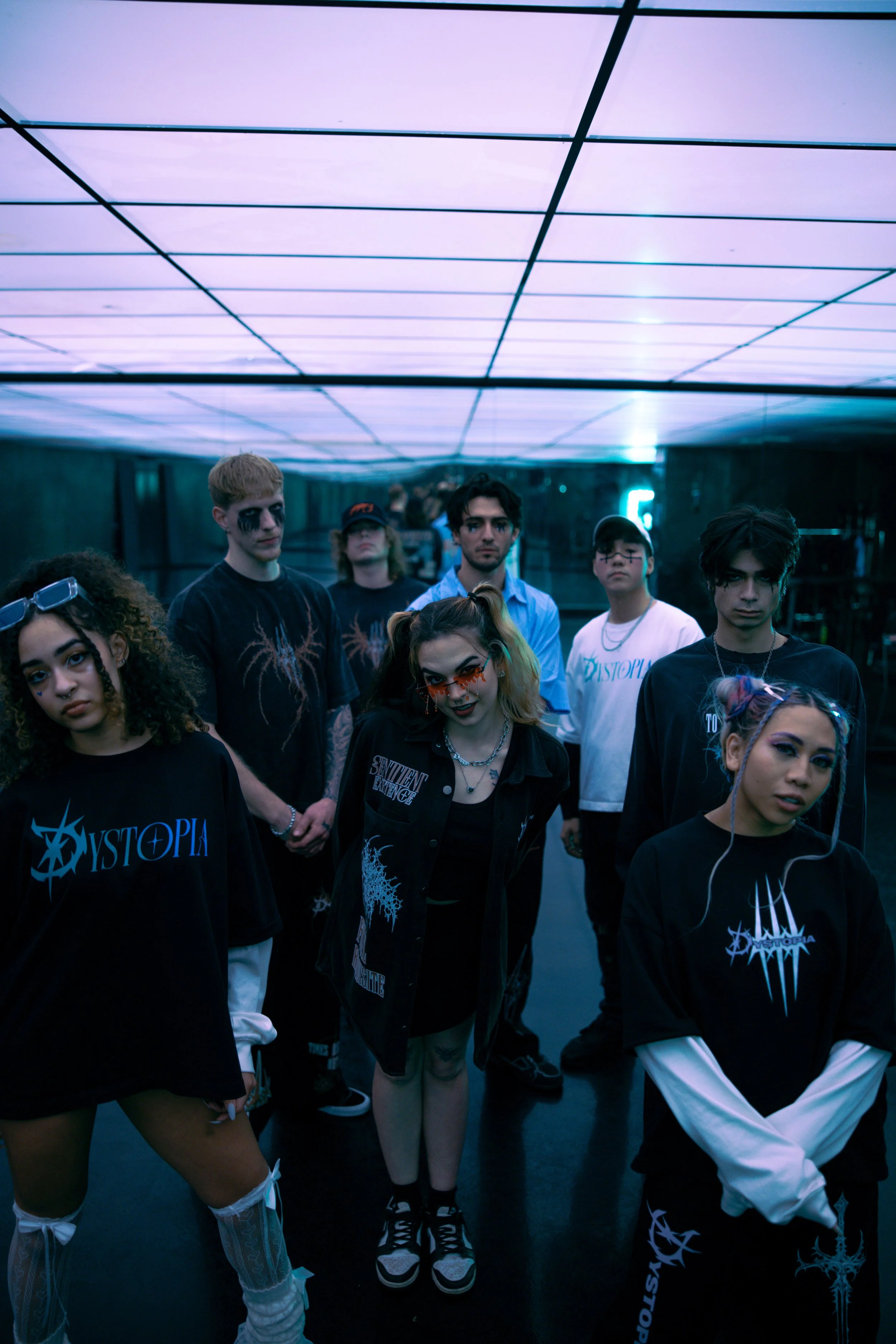 Group of young people in dark, edgy fashion standing in futuristic, neon-lit room.