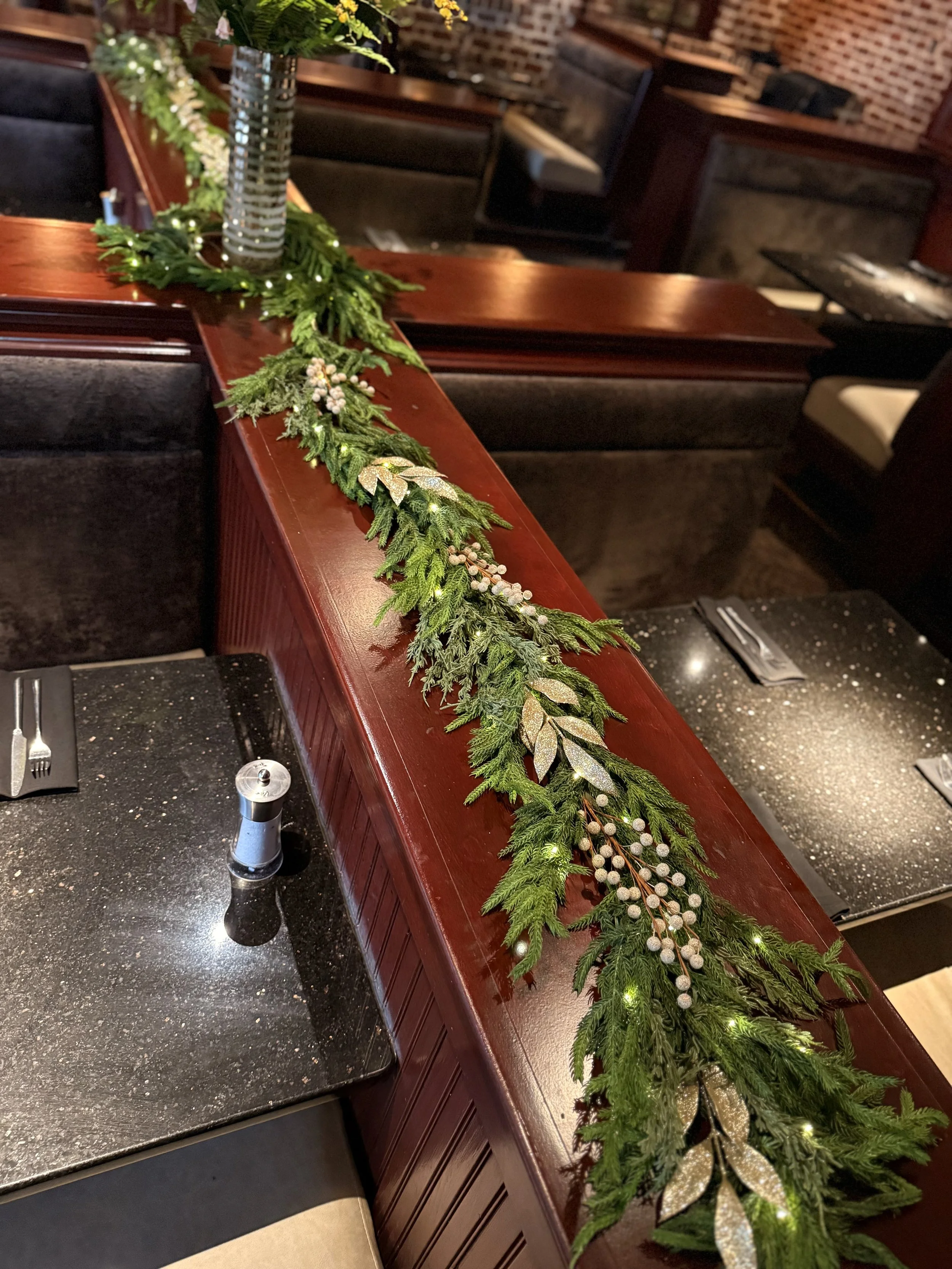 Indoor restaurant booths and tables with festive garland on wood in between tables with lights.
