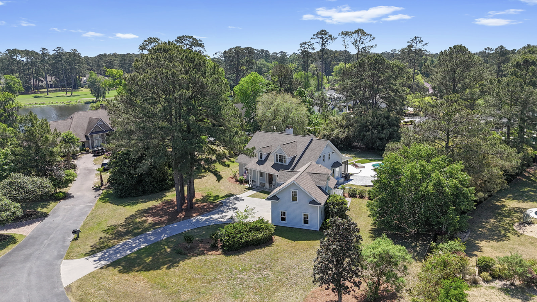 Aerial view of a suburban neighborhood with large houses, surrounded by green trees, a pond, and a backyard with a pool.