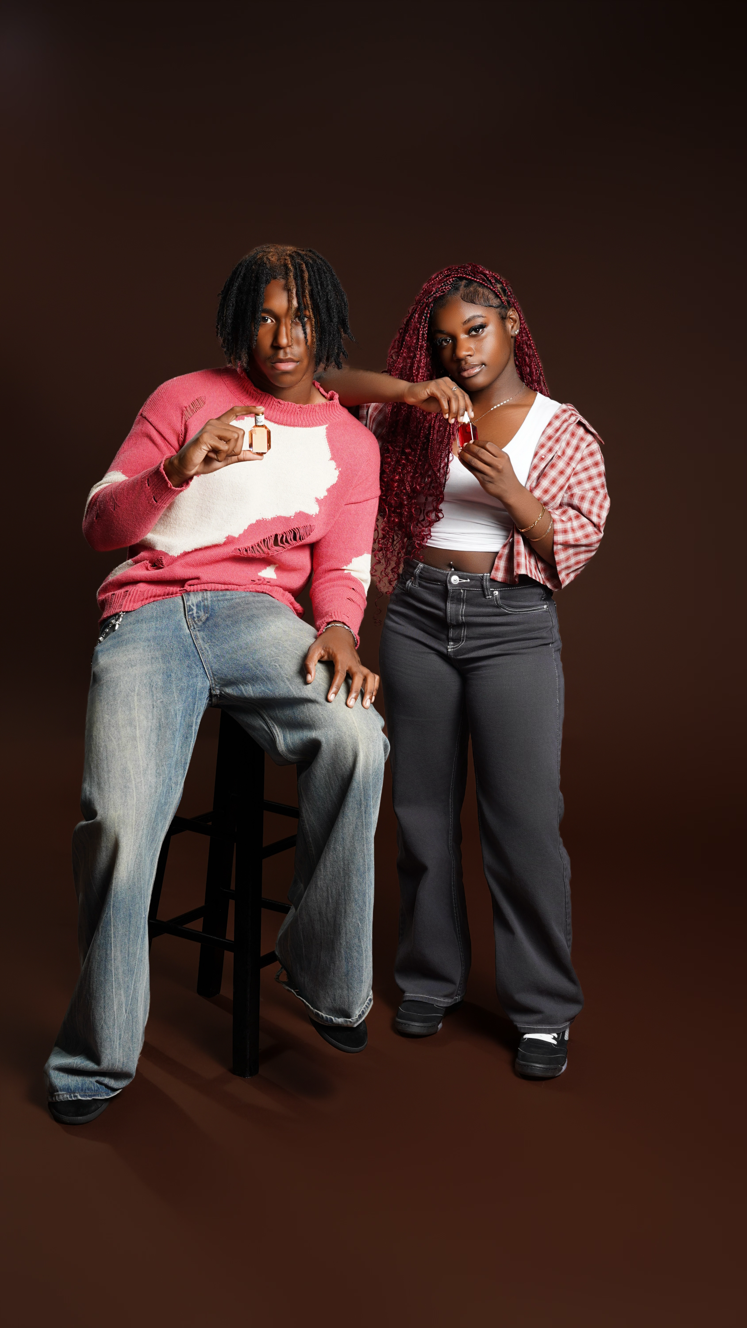 Two young women with dark skin and curly hair standing against a plain dark background, each holding a small bottle.
