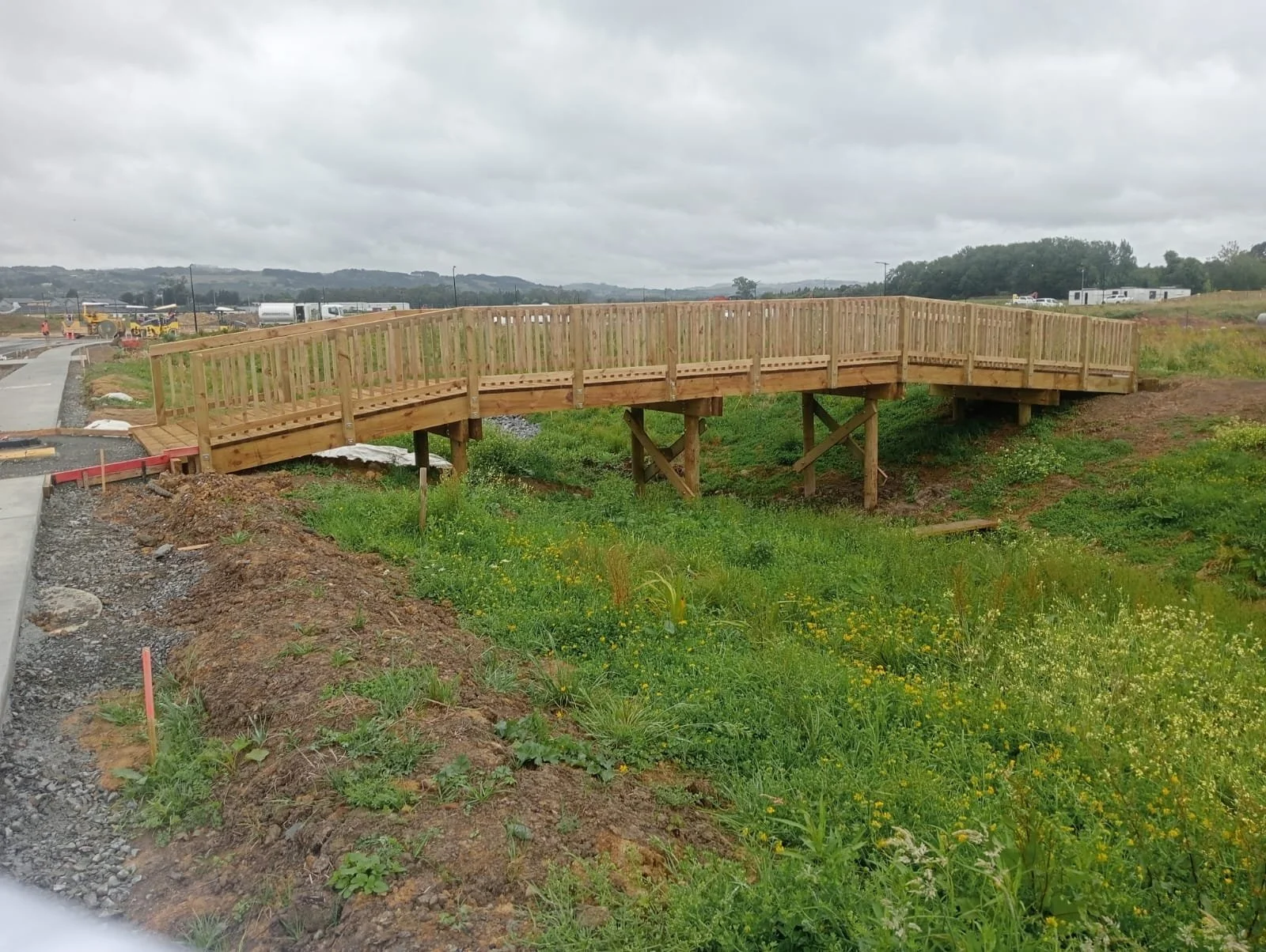 A wooden bridge under construction with scaffolding around it, over a small creek in a grassy area.
