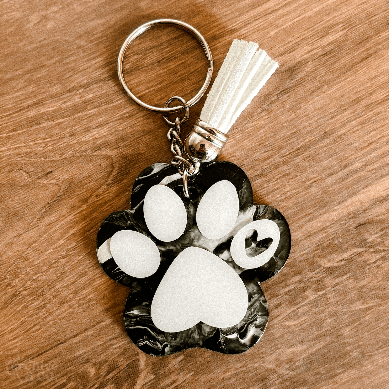 handmade paw print keychain with black and white marbled fur-inspired pattern, white paw details, tassel, and silver keyring