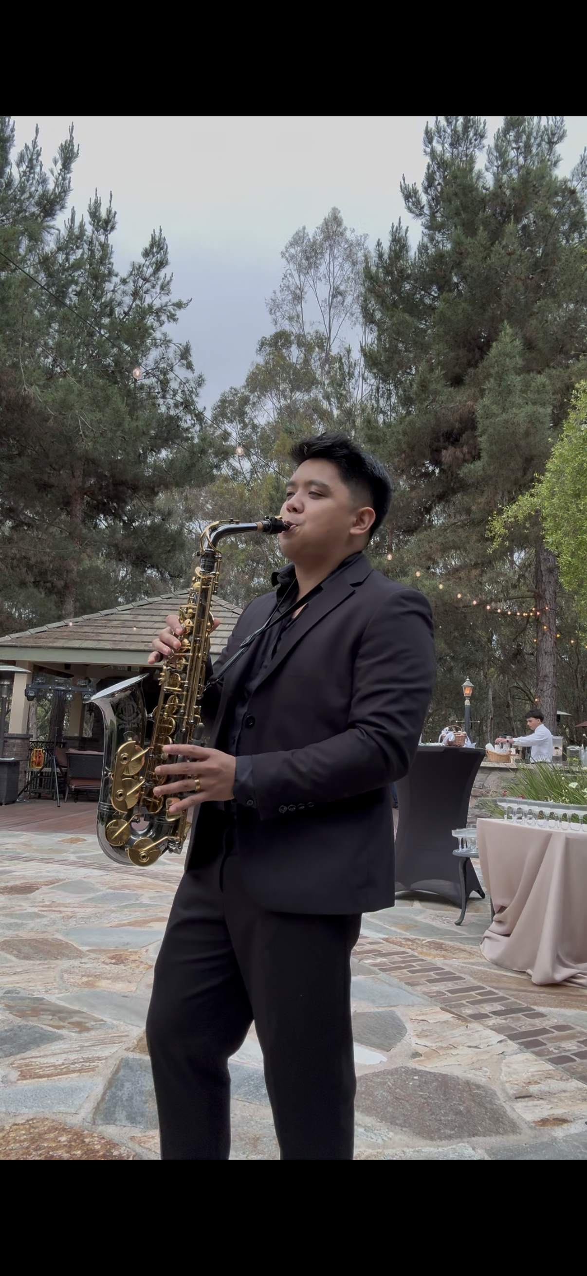 A group of people at a celebration dancing and enjoying live jazz music, with a focus on a young man playing the saxophone, surrounded by happy guests.