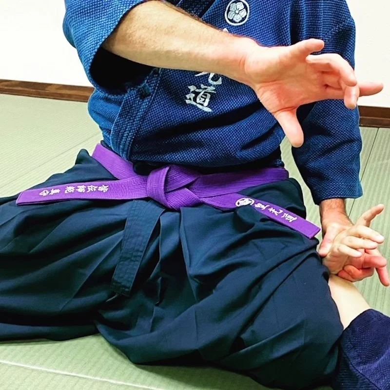 KoKoDo Jujutsu Vancouver JiuJitsu instructor in traditional gi and purple belt demonstrates a technique on a student lying on a tatami mat.