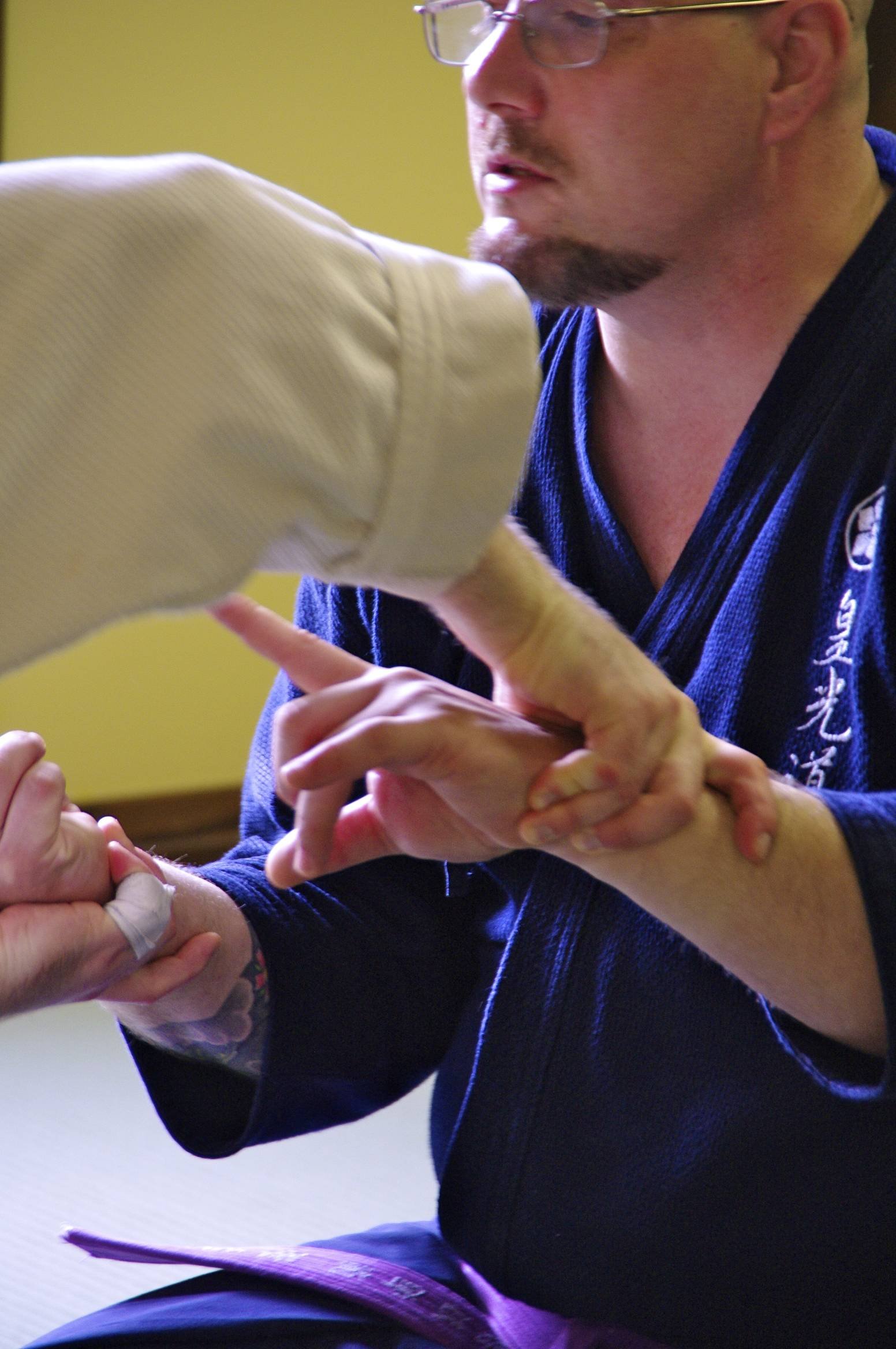 A person performing aiki  jujutsu practicing an arm lock technique with another person, during a martial arts training session.
