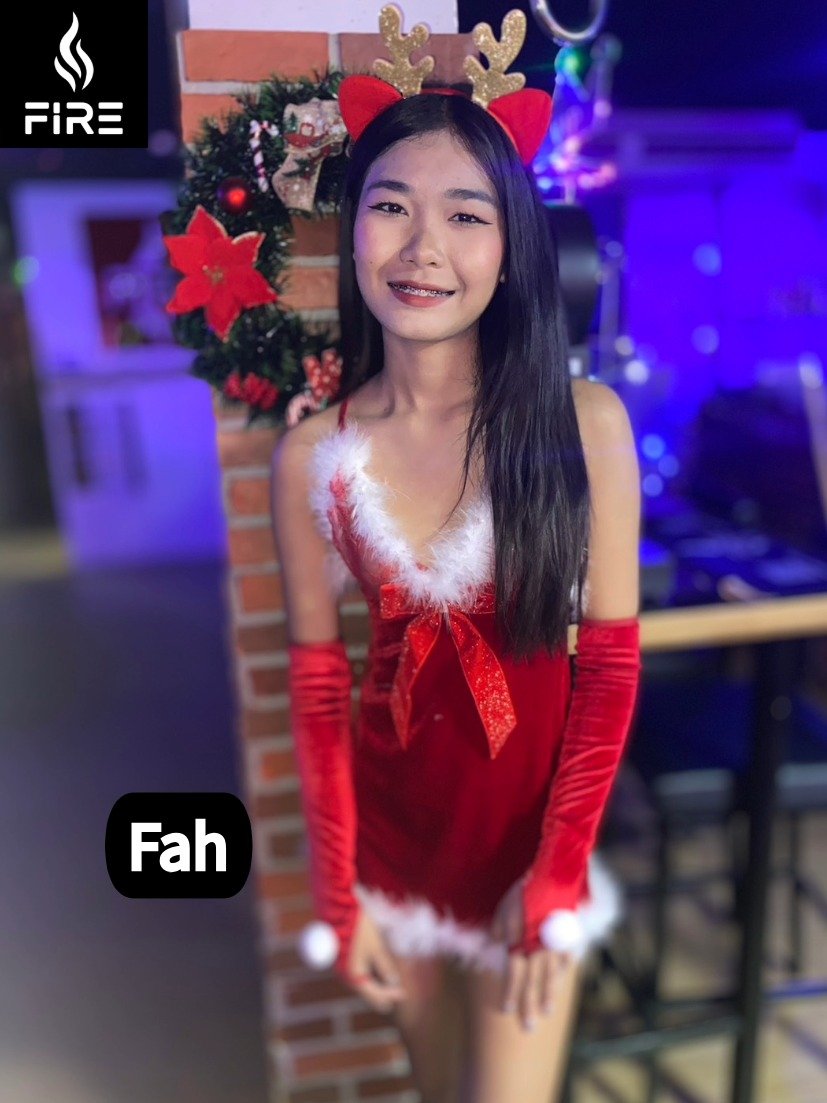 Young woman in a festive Christmas outfit with reindeer antlers and a red dress with white fur trim, standing in front of a decorated Christmas wreath.