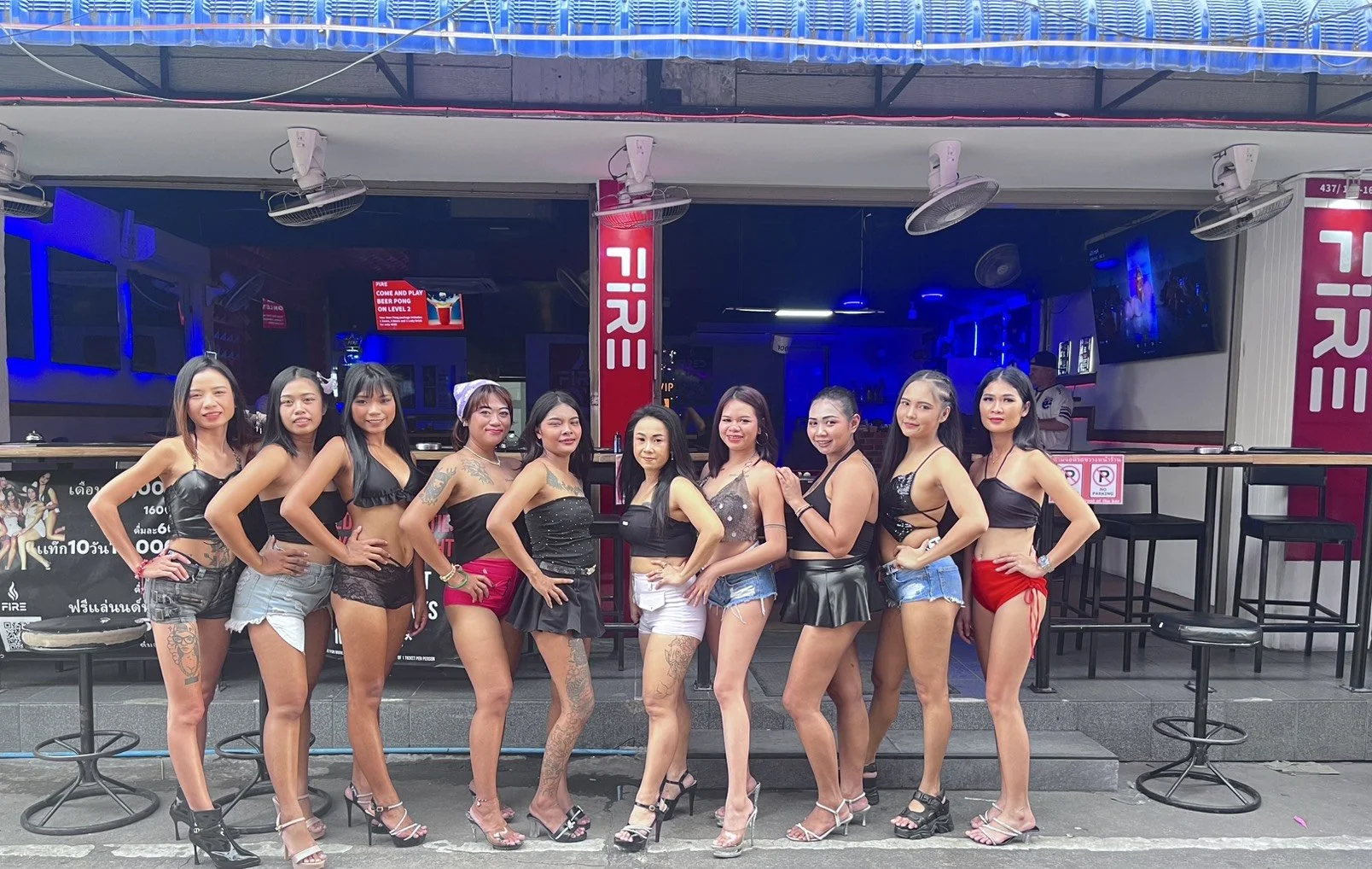 Group of ten women in revealing outfits posing outside a nightclub.