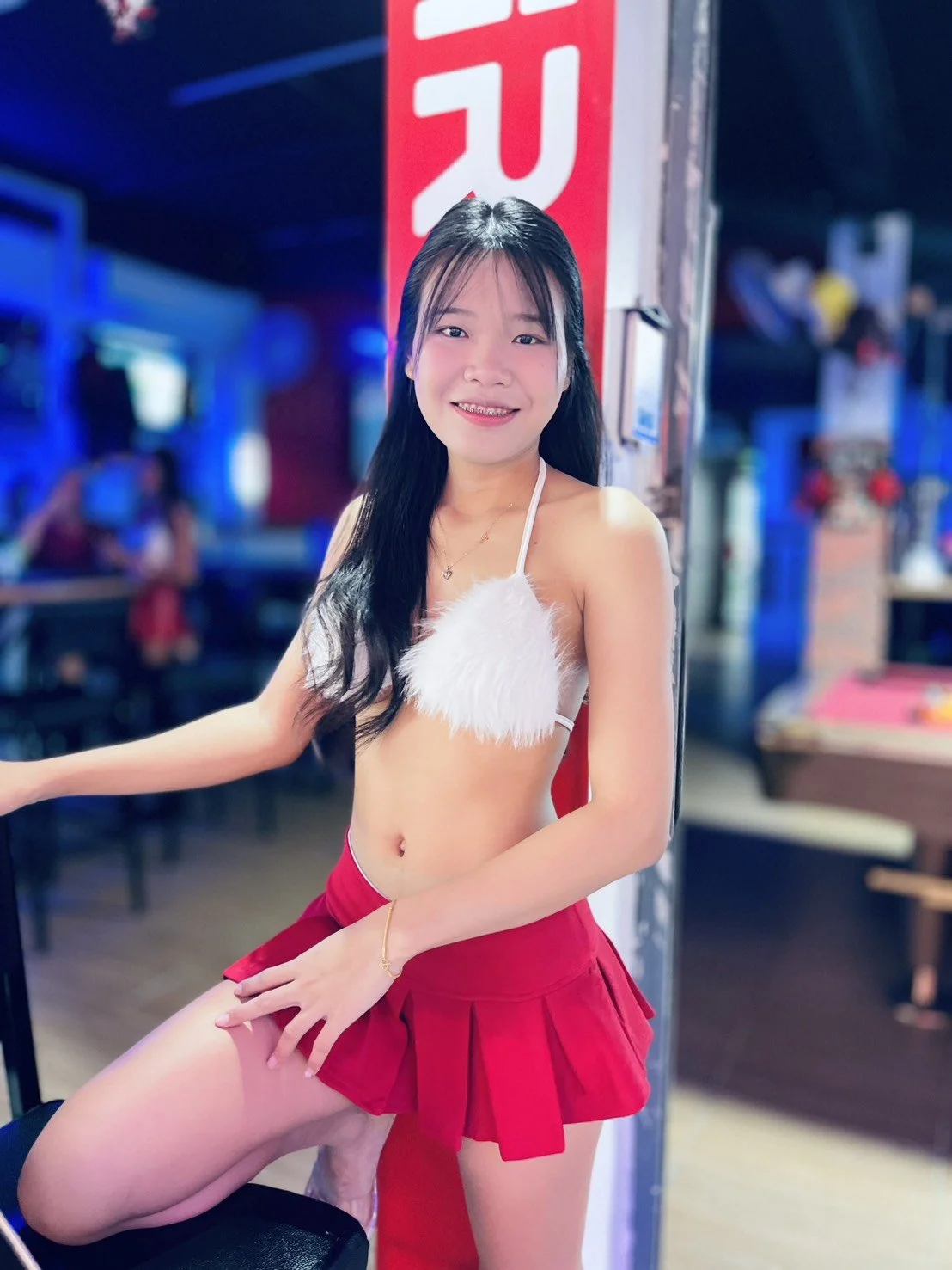 A young woman in a white furry top and a red skirt posing and smiling in a lively, colorful indoor venue.