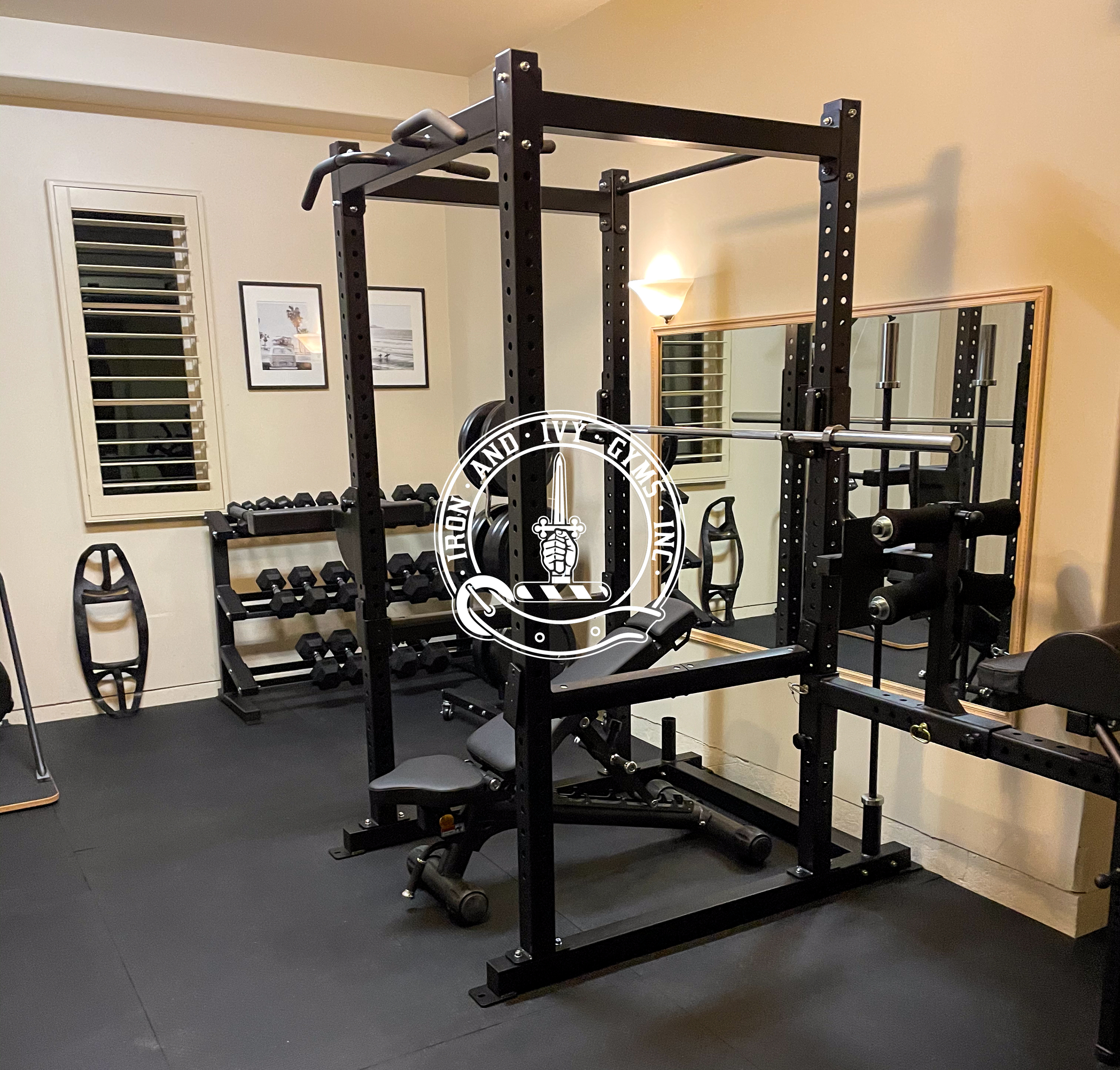 Home gym with black metal power rack, adjustable bench, dumbbell rack with weights, mirror, wall-mounted lights, and wall decorations.