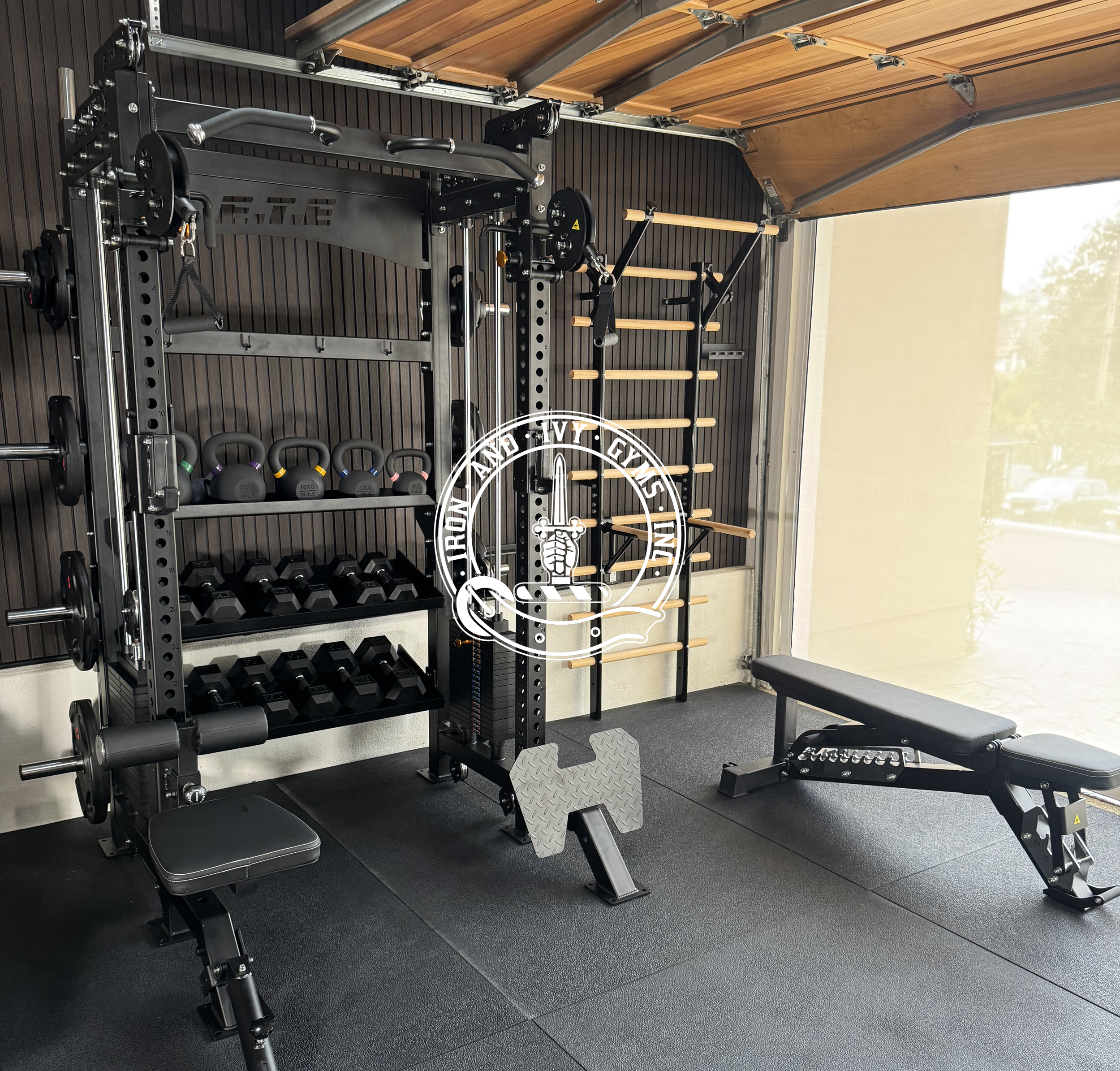 Strength training gym with various equipment including a squat rack, dumbbells, kettlebells, an adjustable weight bench, a wall-mounted wooden ladder, and a wall-mounted pull-up bar, in a room with rubber flooring and a large window.