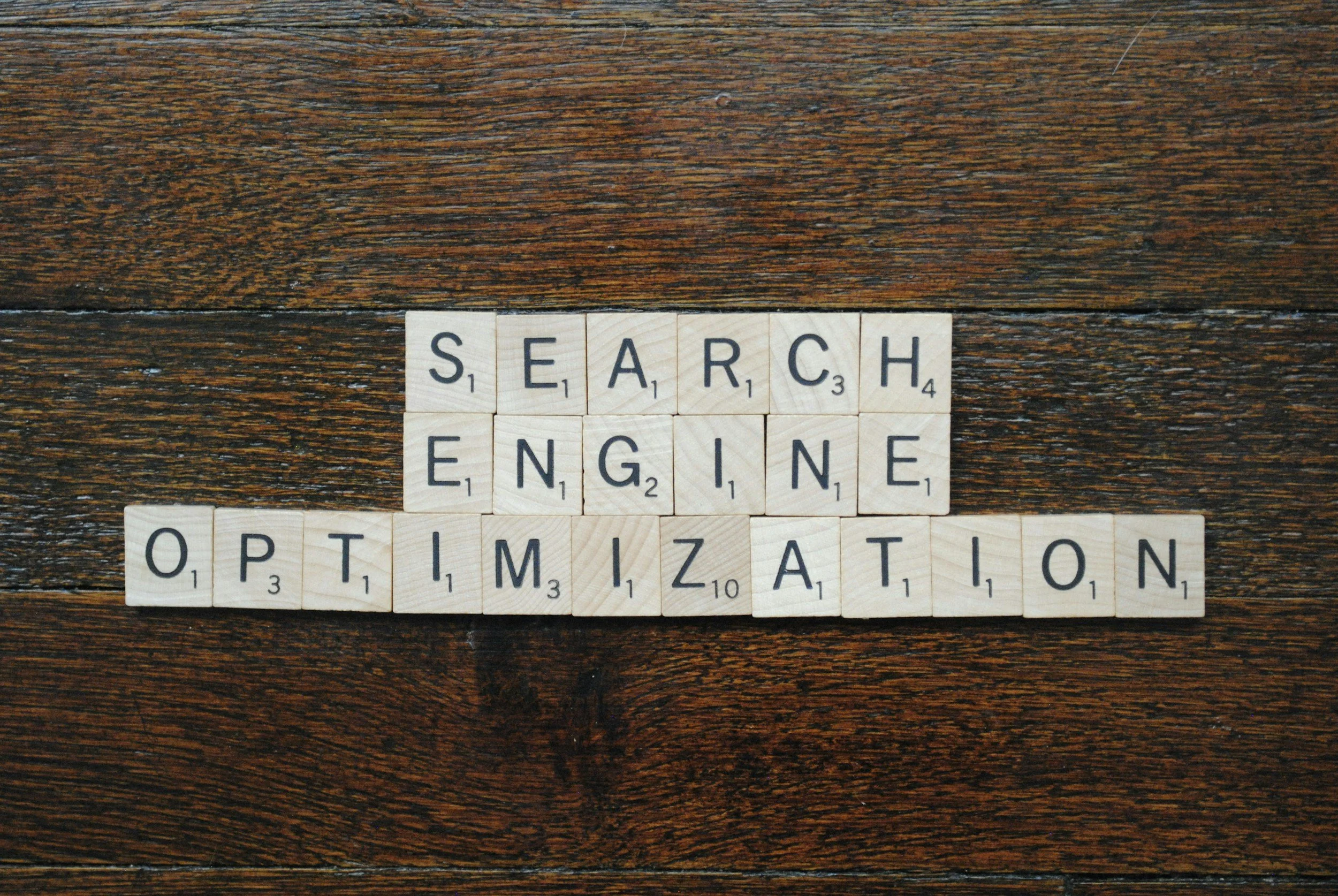 Scrabble tiles arranged to spell 'SEARCH ENGINE OPTIMIZATION' on a wooden surface.