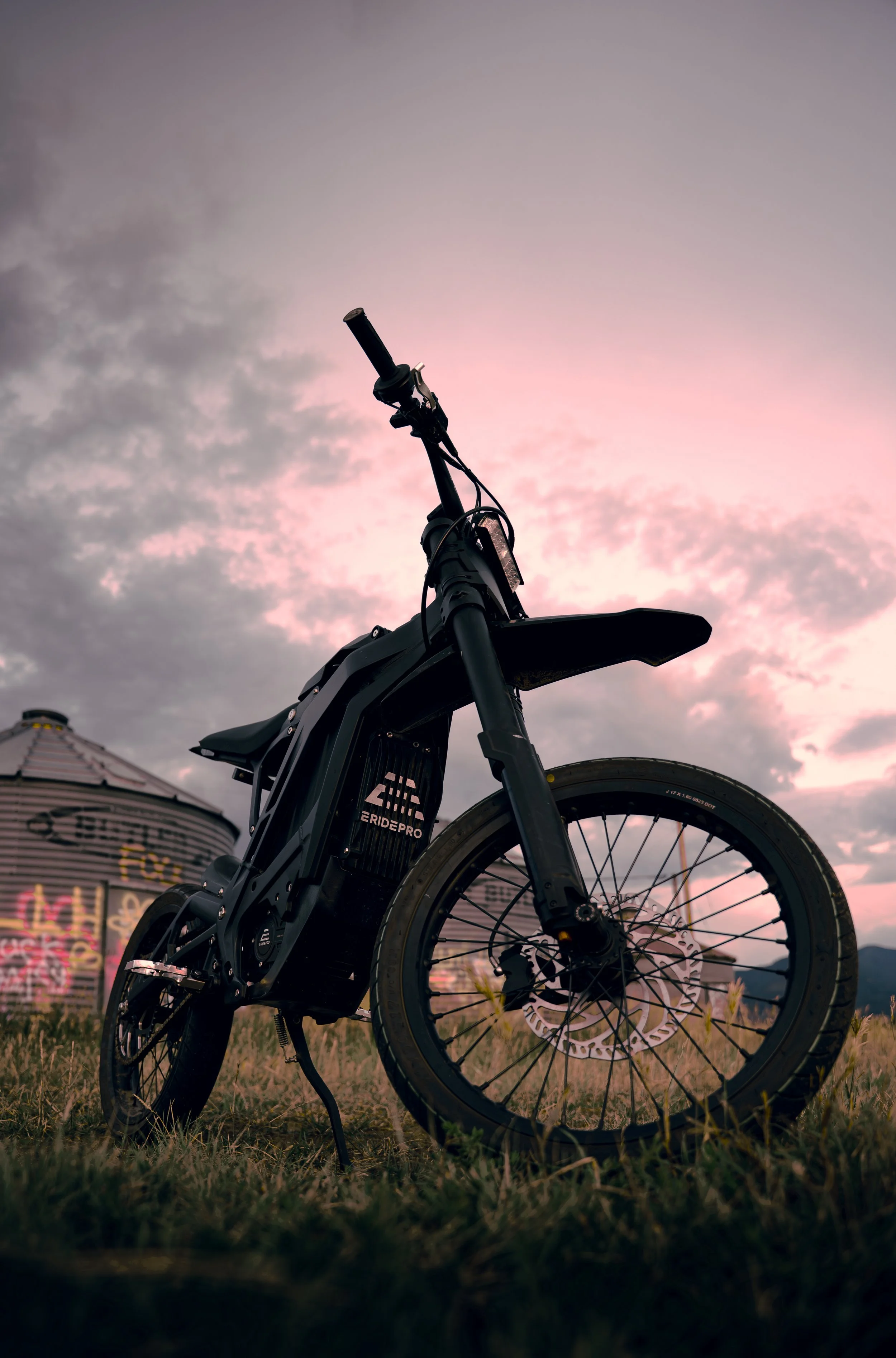Black electric bike outdoors at sunset with graffiti-covered building in background.