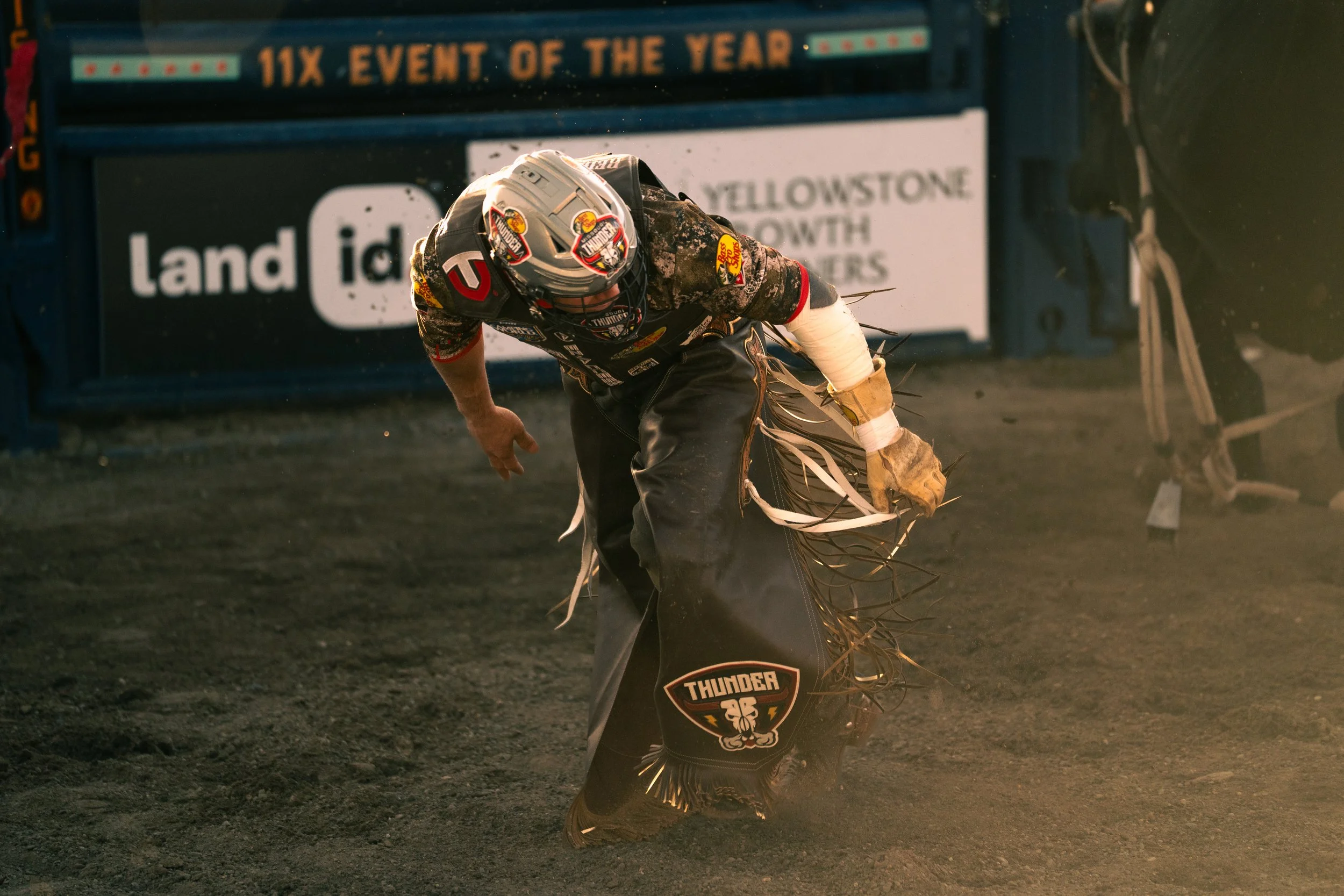 A dirt track motorcycle racer falling or kneeling, wearing a helmet and racing gear, with the ground kicking up dust visible.
