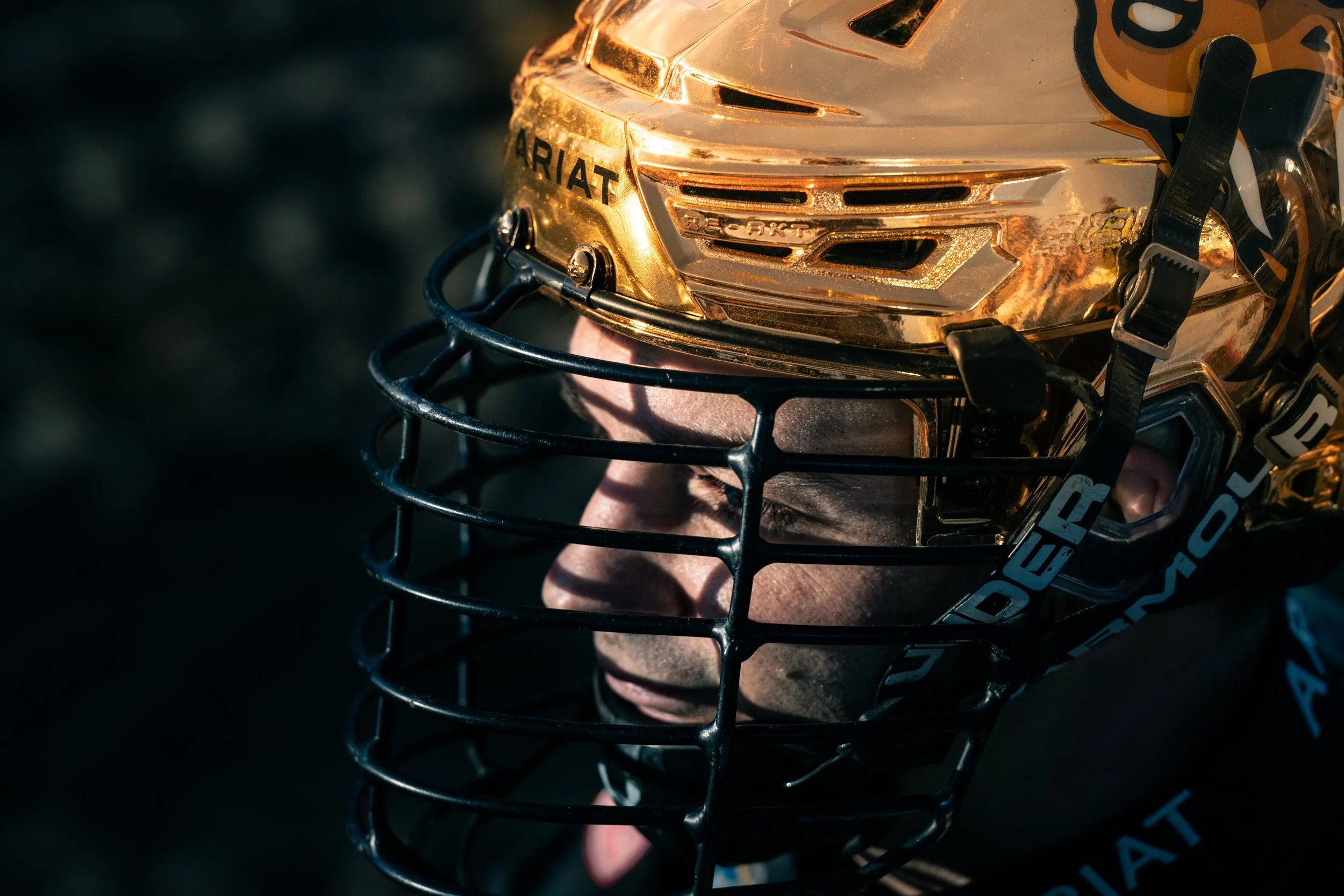 Close-up of a person wearing a gold hockey helmet with a black cage faceguard, with their eyes closed.