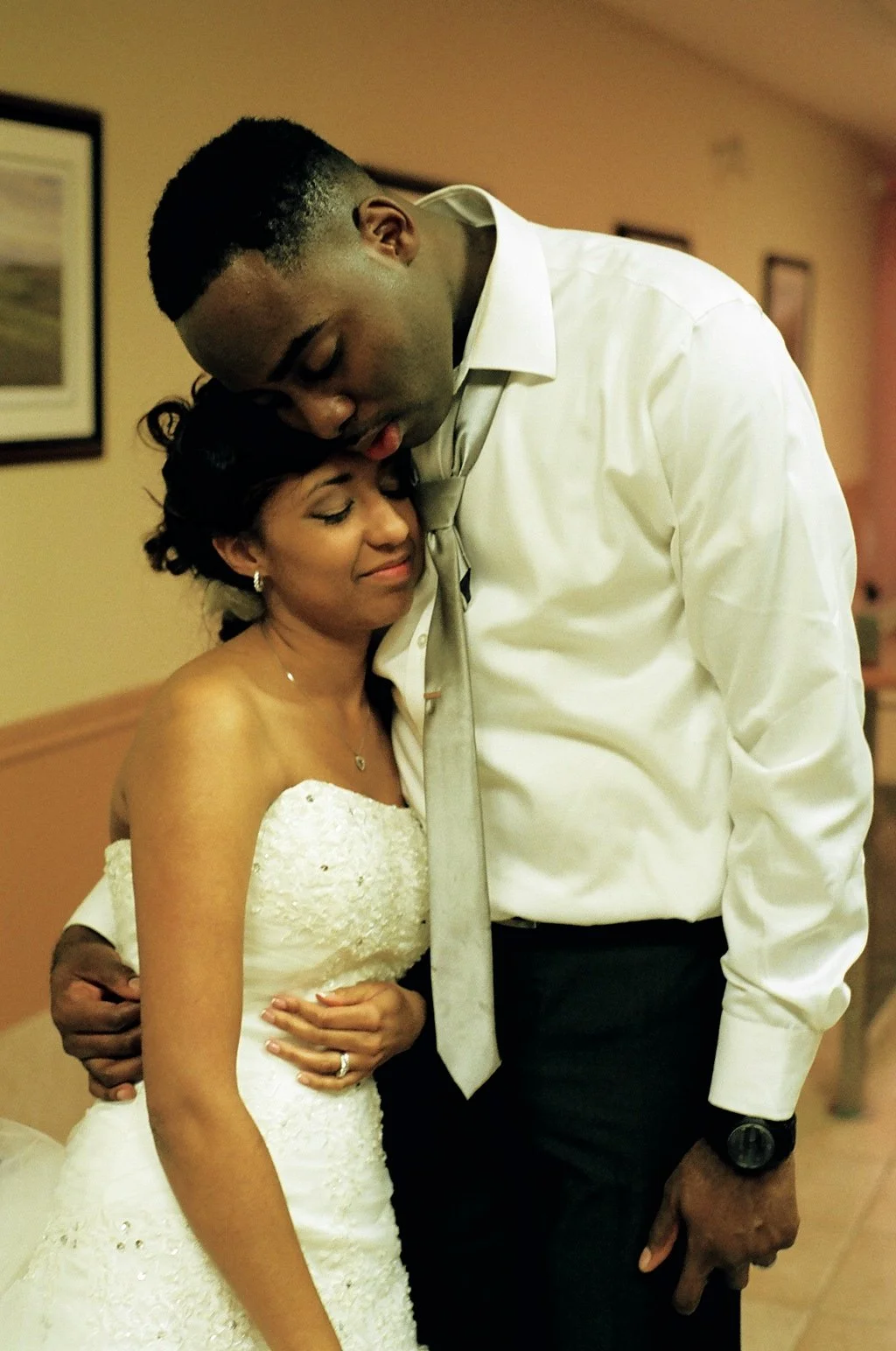 A bride and groom sharing a loving moment, with the groom resting his head on the bride's head as she smiles peacefully.