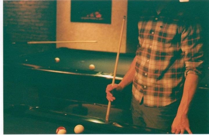 Person in a plaid shirt playing pool with a cue stick.