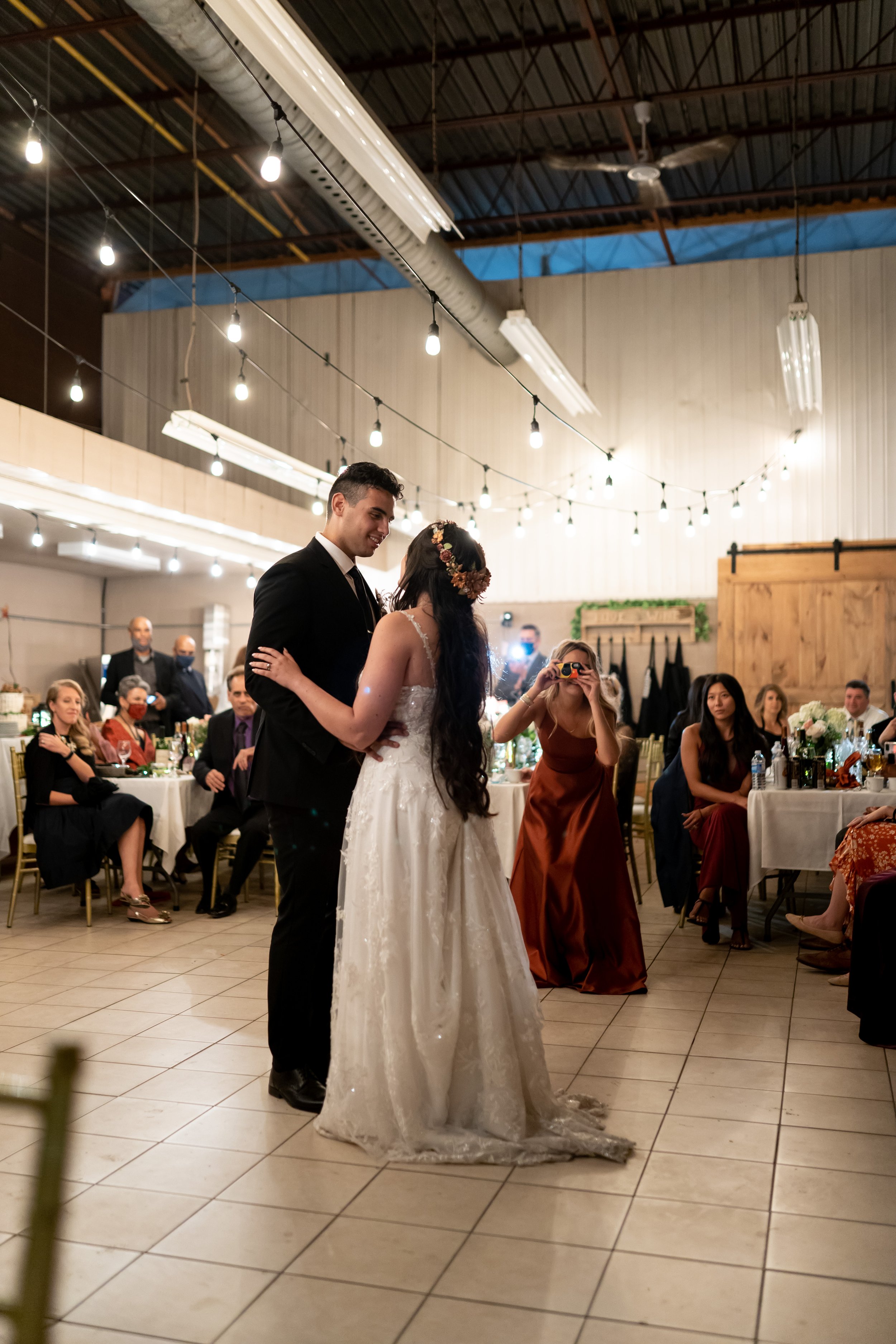 A bride and groom are dancing at their wedding reception in a decorated hall filled with seated guests as they share their first dance.