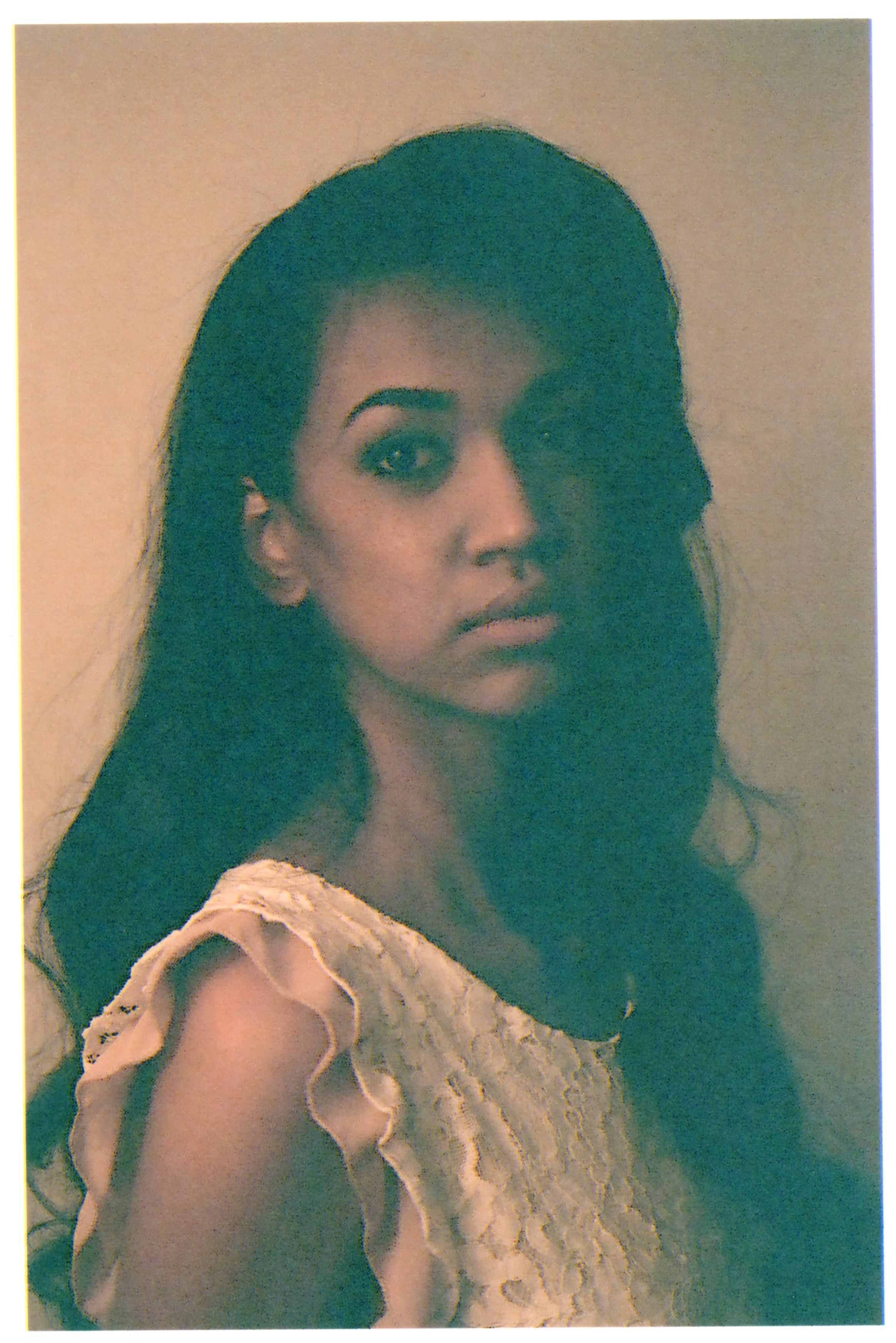A woman with dark hair styled in loose waves, wearing a light-colored, ruffled sleeveless blouse, looking over her shoulder against a plain background.