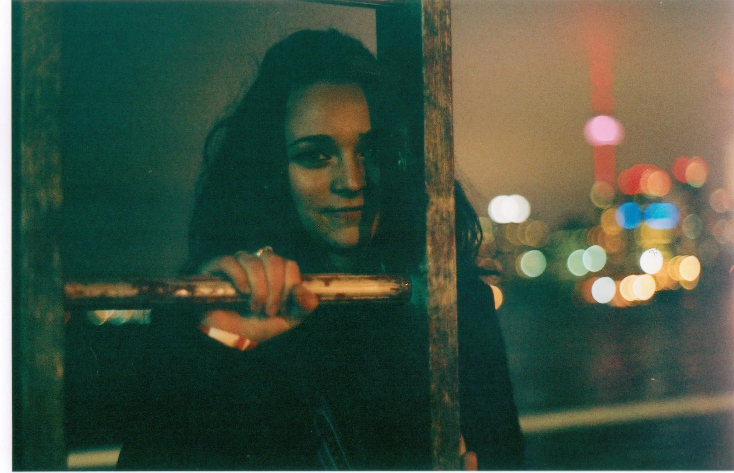 Woman taking a selfie in a mirror, with city lights blurred in the background at night.