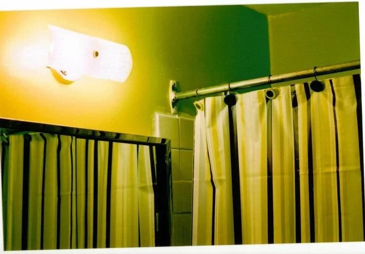 Bathroom with green walls, a white light fixture above, and yellow and dark striped shower curtains hanging from a metal rod.
