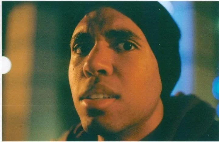 Close-up of a young man with dark hair, wearing a black beanie, looking concerned or surprised.