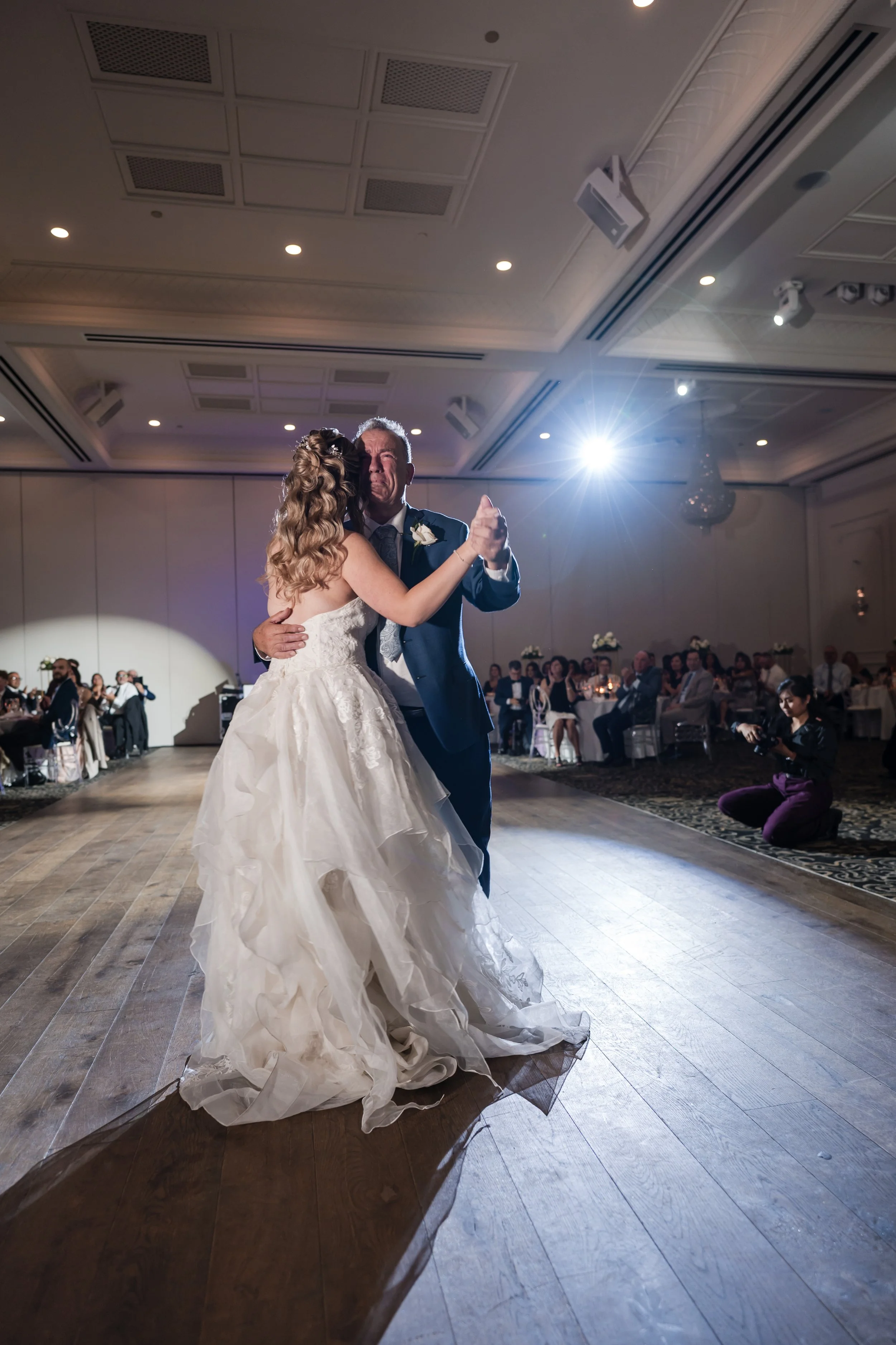 A bride and groom sharing a dance at their wedding reception, with seated guests watching in the background.