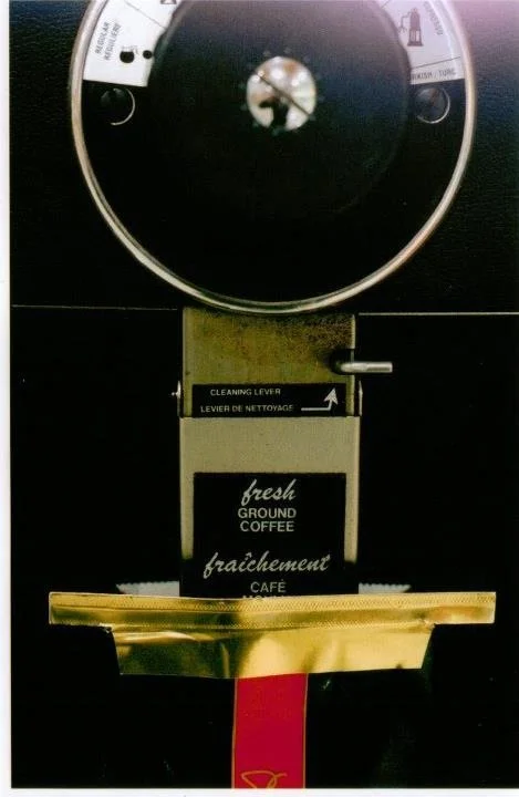 Close-up of a coffee vending machine with a selection panel and a gold-colored coffee cup holder.