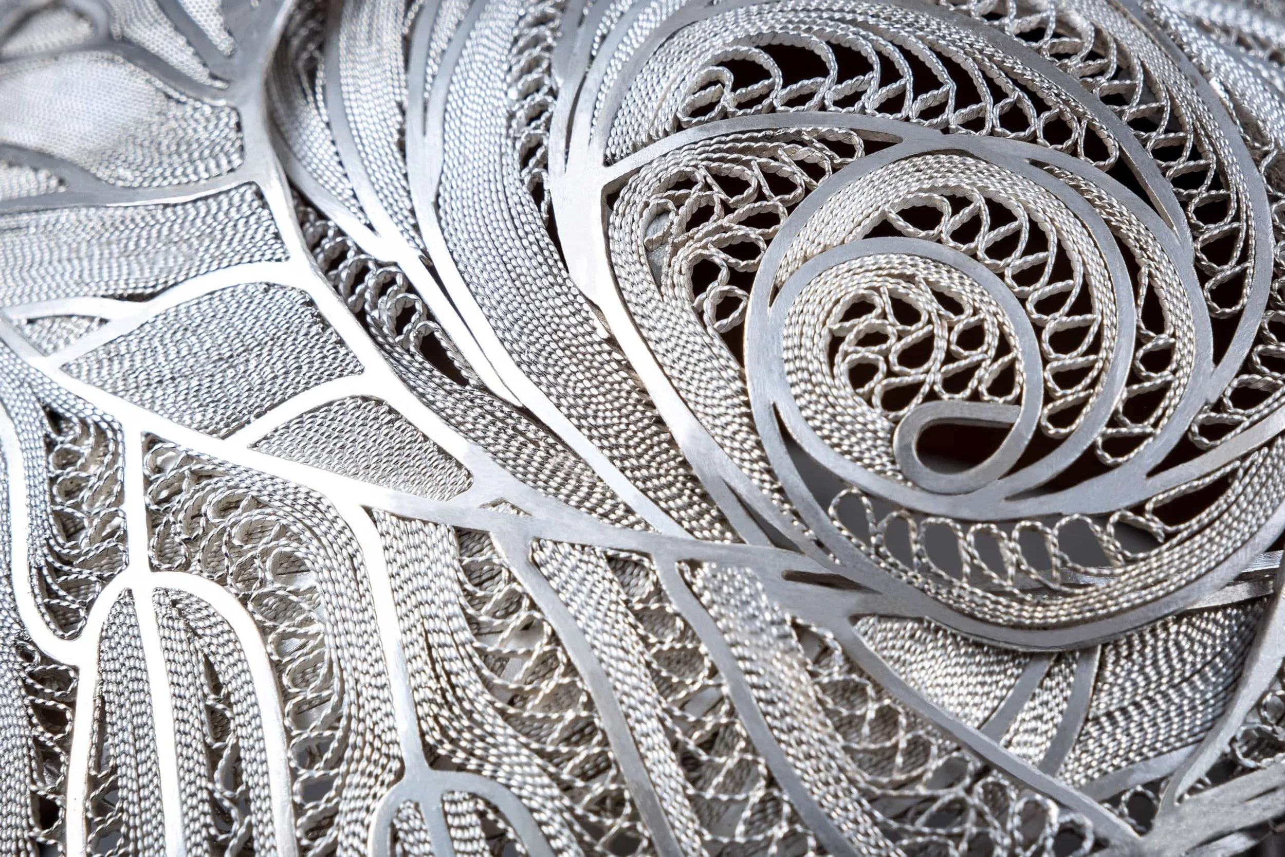 Close-up of intricate silver jewelry with detailed filigree and mesh design.