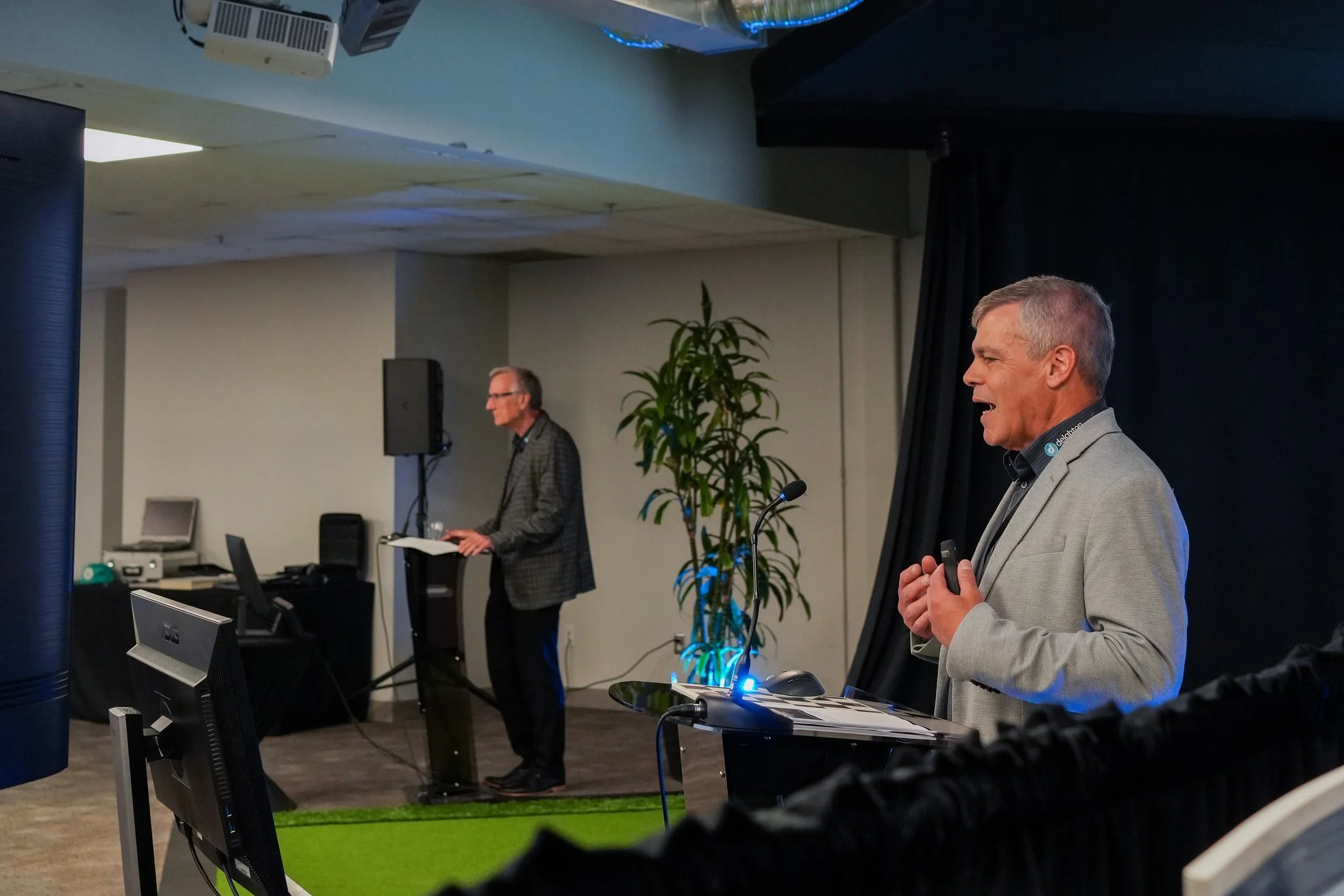 Gary in the foreground presenting at a podium and Jeff can be seen in the background.