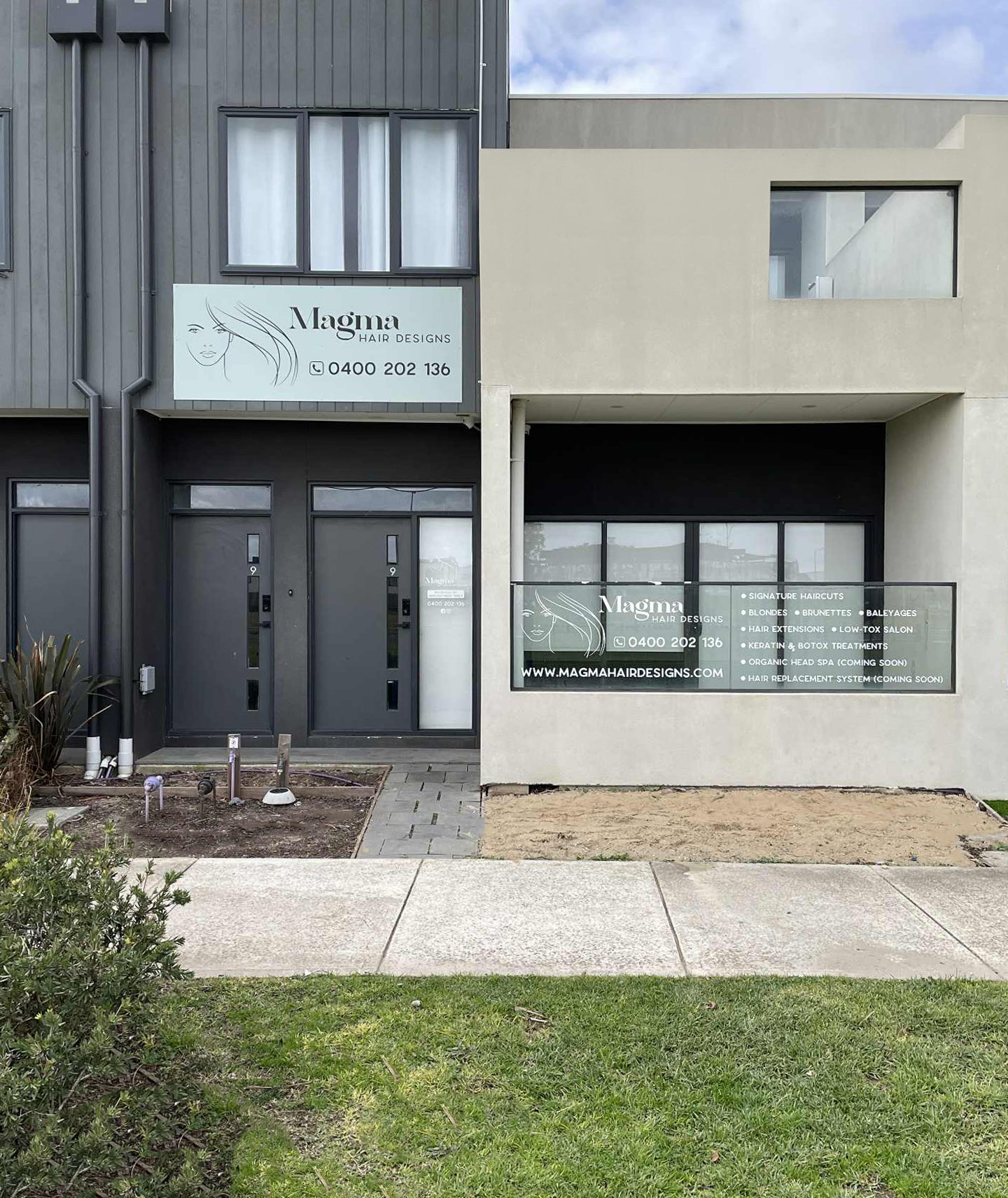 The storefront of a hair salon called Magma Hair Designs, featuring a sign with a woman's face and flowing hair illustration, the shop's name, contact number, and a large window displaying services such as haircuts, balayage, hair extensions, keratin