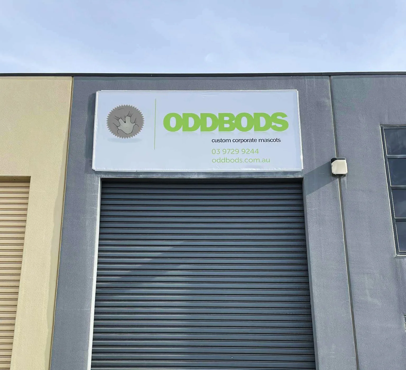 Sign for ODDBODS custom corporate mascots above a closed gray roller door.