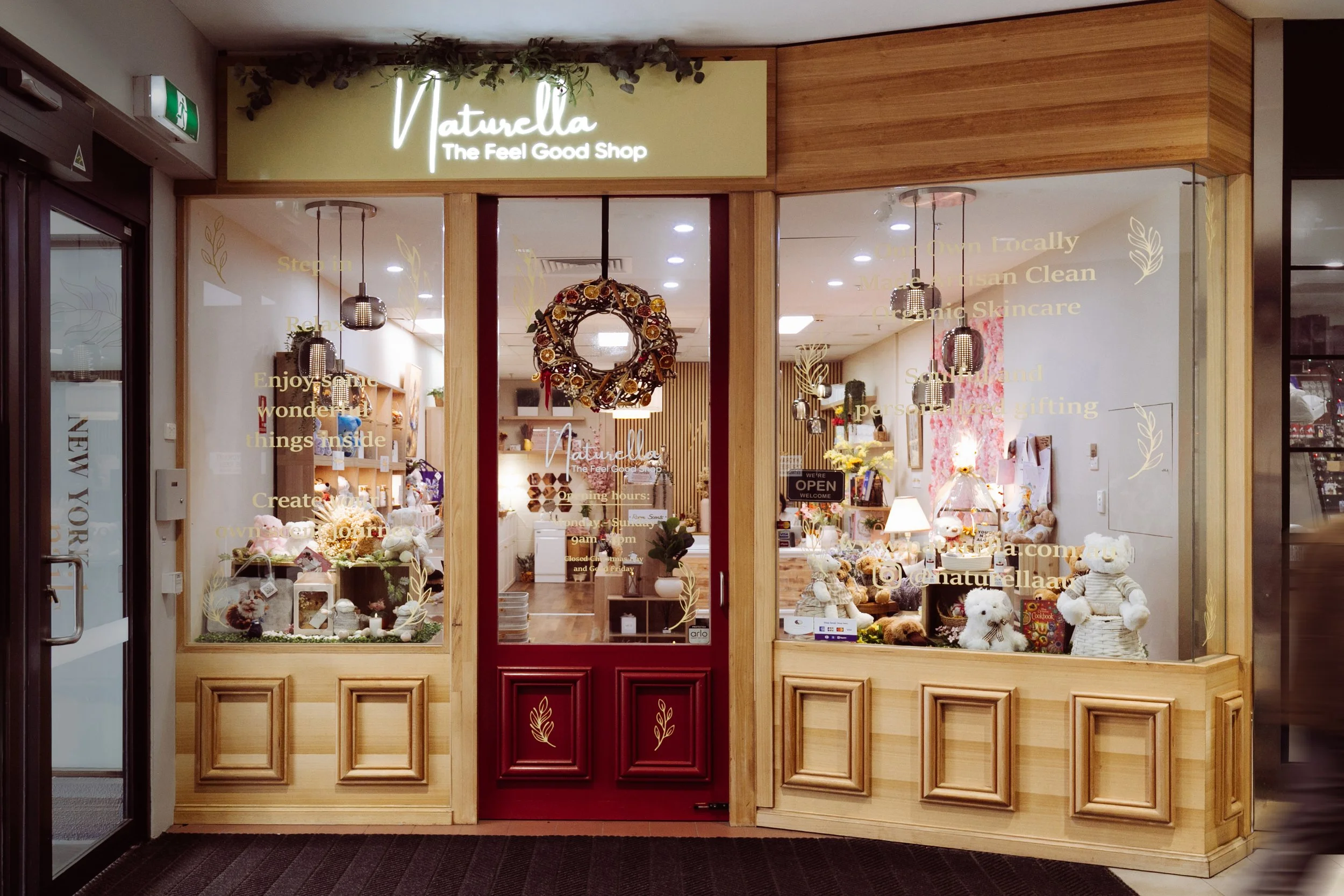 Storefront of Naturella, a shop with a glass front showcasing plush toys and home decor items; wooden framing and a wreath on the door.