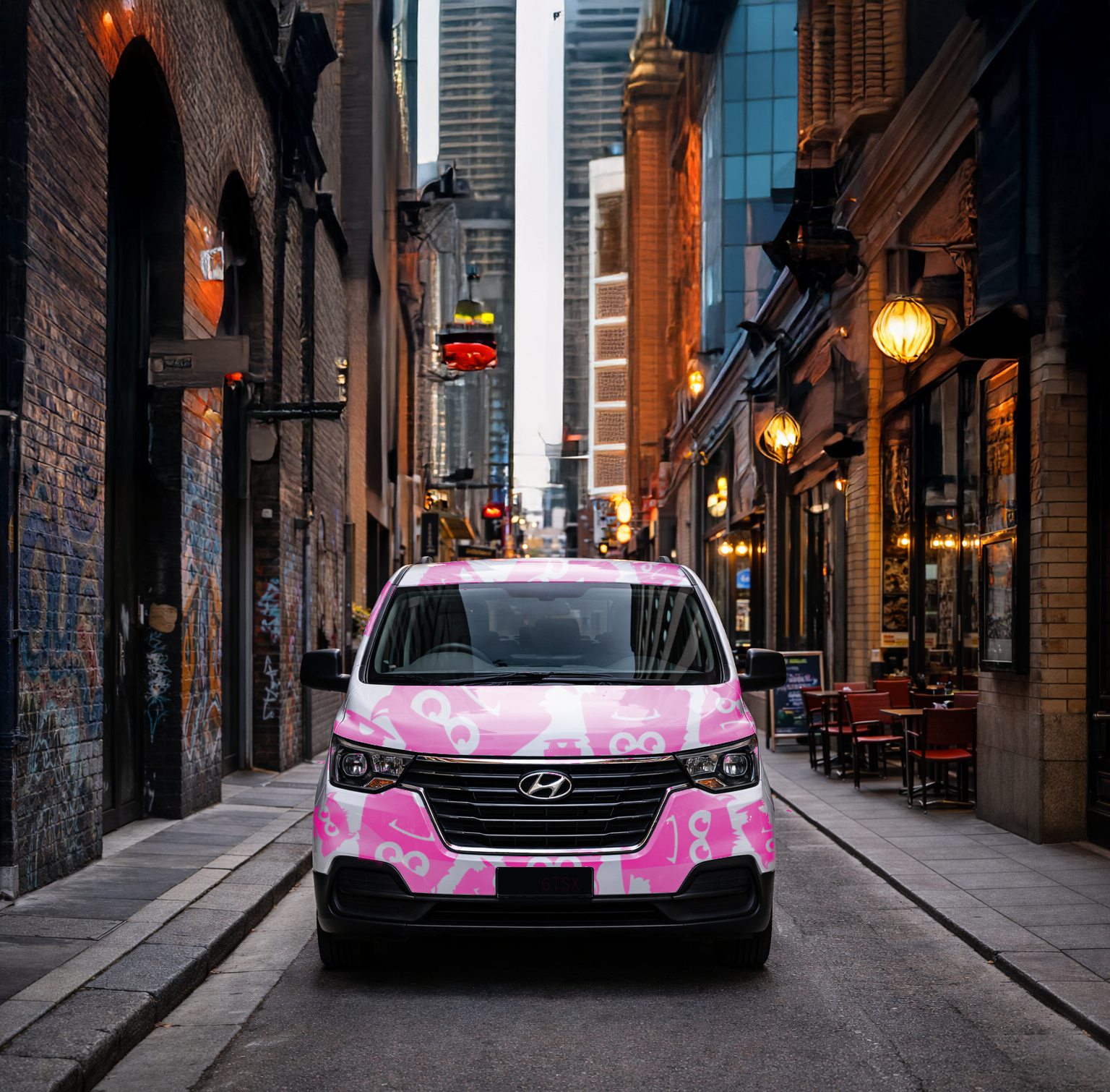 A pink and white Hyundai van parked in a narrow city alleyway surrounded by brick buildings, with outdoor seating on the right and illuminated street lamps at dusk.
