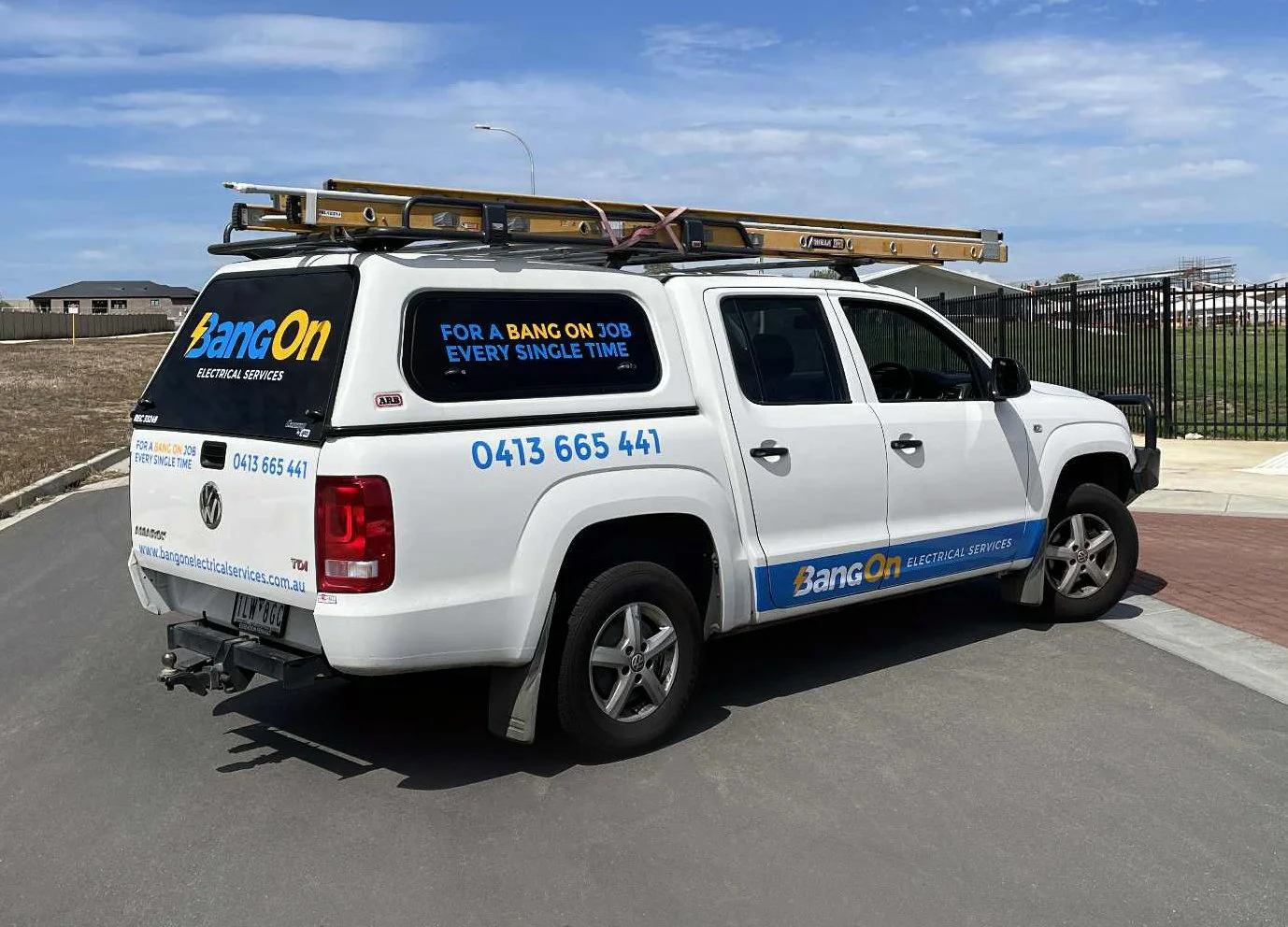 White service vehicle with company branding for Bang On Electrical Services, featuring a roof ladder, company contact information, and branding on the vehicle's side and rear windows.